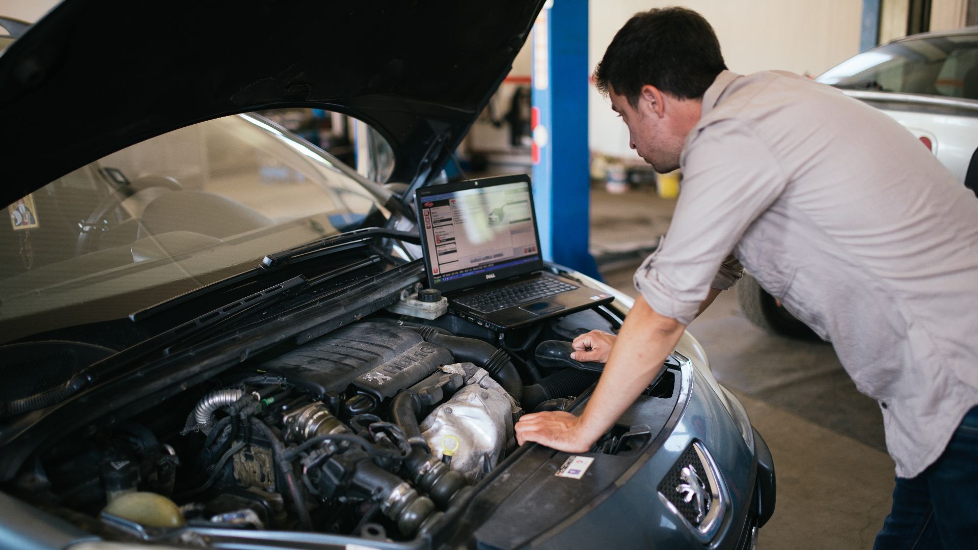 Young mechanic with laptop doing car diagnostic at automobile repair shop close