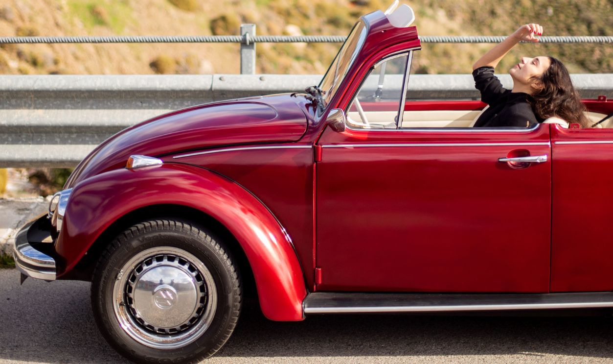 A woman enjoys a drive in a red vintage convertible against a scenic backdrop, capturing a carefree adventure.