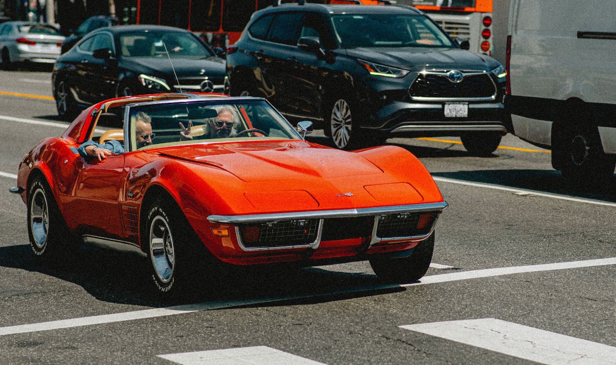 Classic red convertible driving through vibrant city with busy traffic