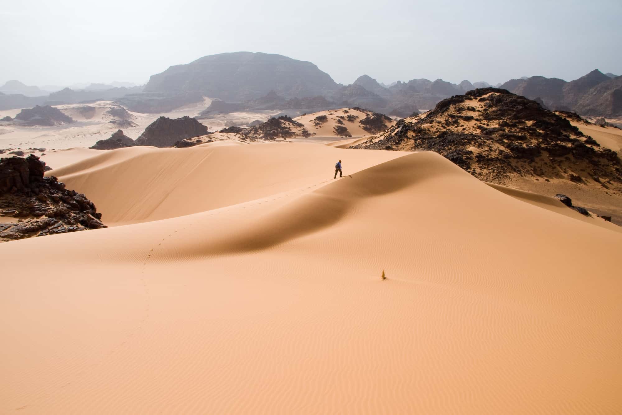 Part of the Sahara Desert in Libya, man walking on the dune, surrounded with hills