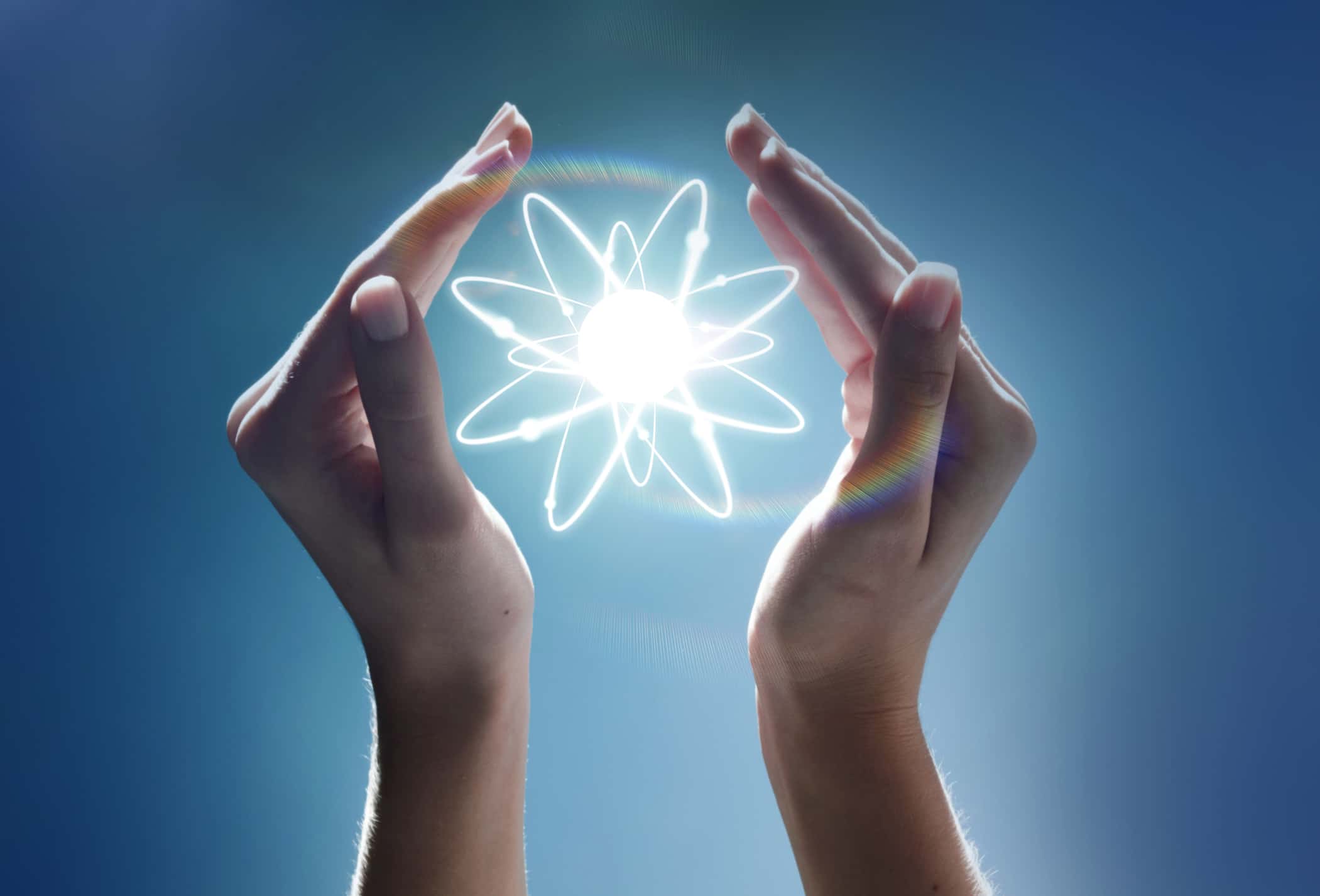 Hands cupping a glowing atom in the studio.
