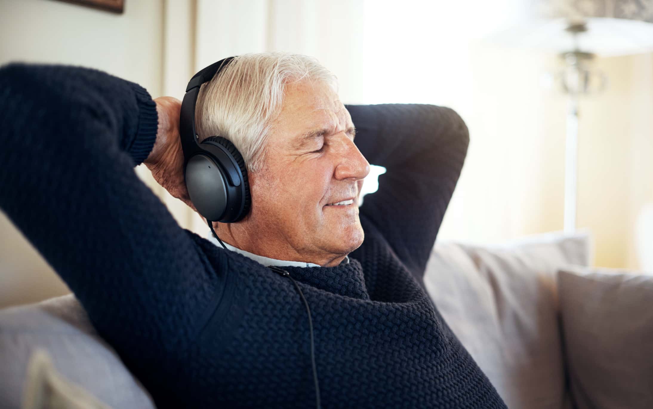 Cropped shot of a senior man wearing dark blue shirt listening to music with headphones on at home