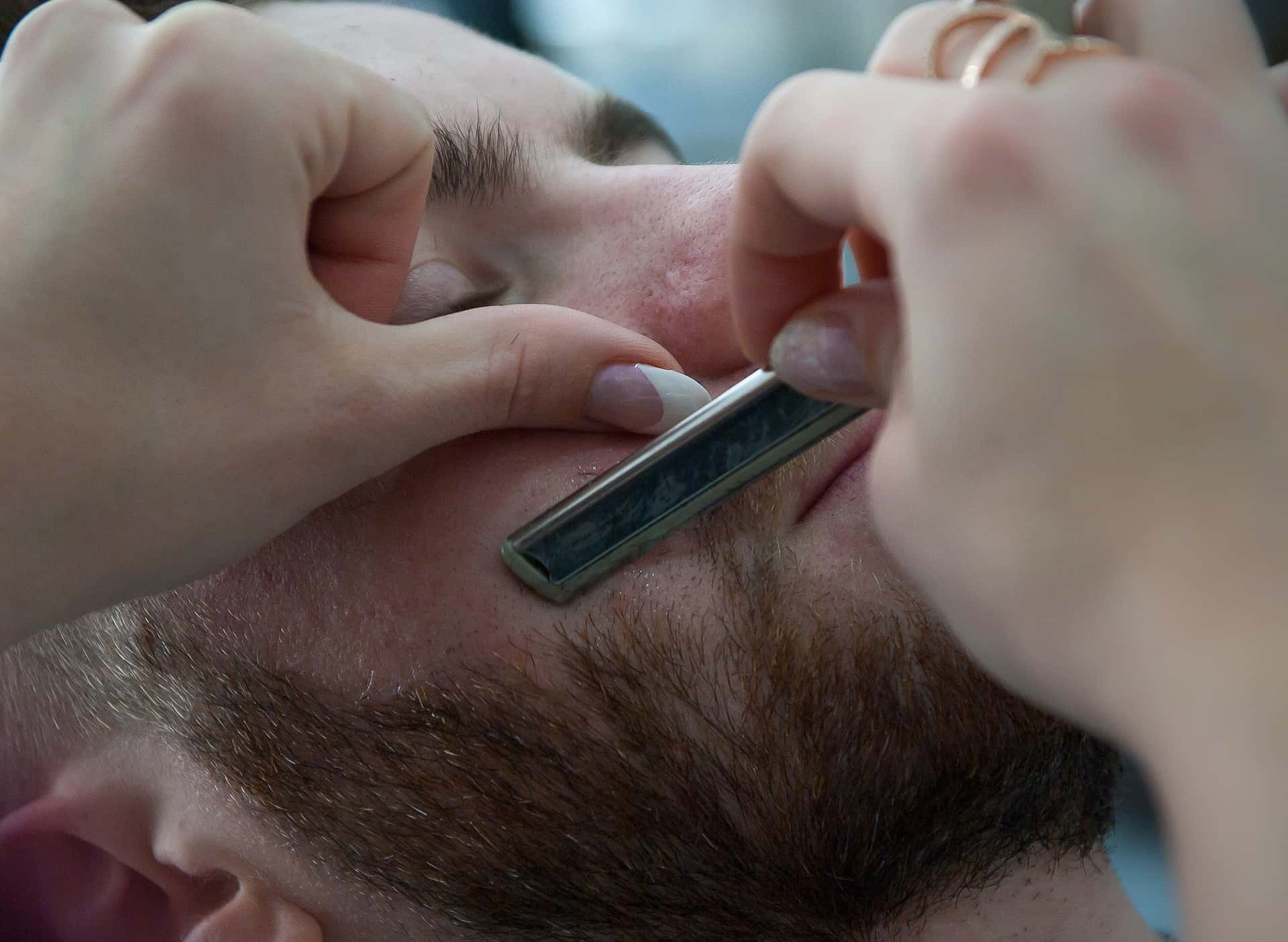Close-up photo of a Barber hands shaving other man beard