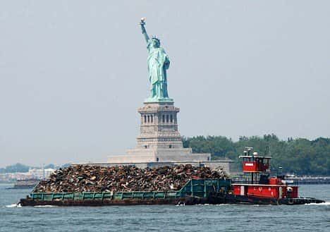 A tug boat pushes a garbage barge past the Statue of Liberty