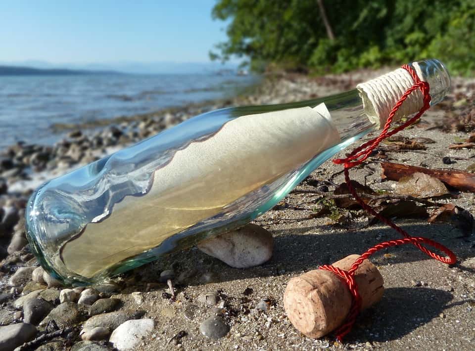 Photo Depicting a Message in a bottle with open cork placed on a beach