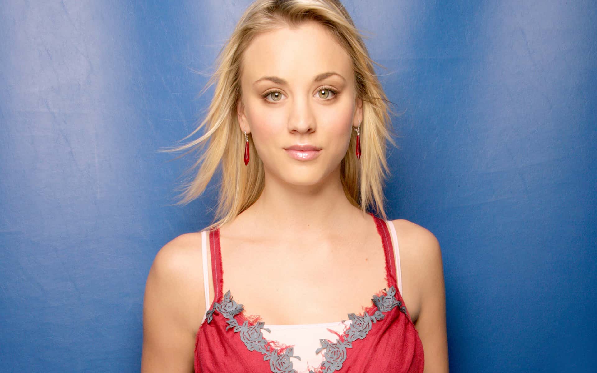 Kaley Cuoco in red tank top and earrings facing the camera