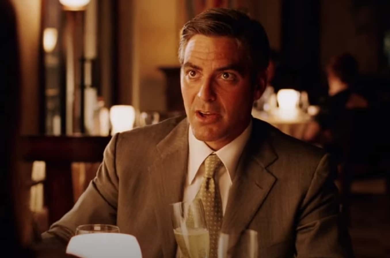 Screenshot of George Clooney seating on the table - from  Intolerable Cruelty (2003)