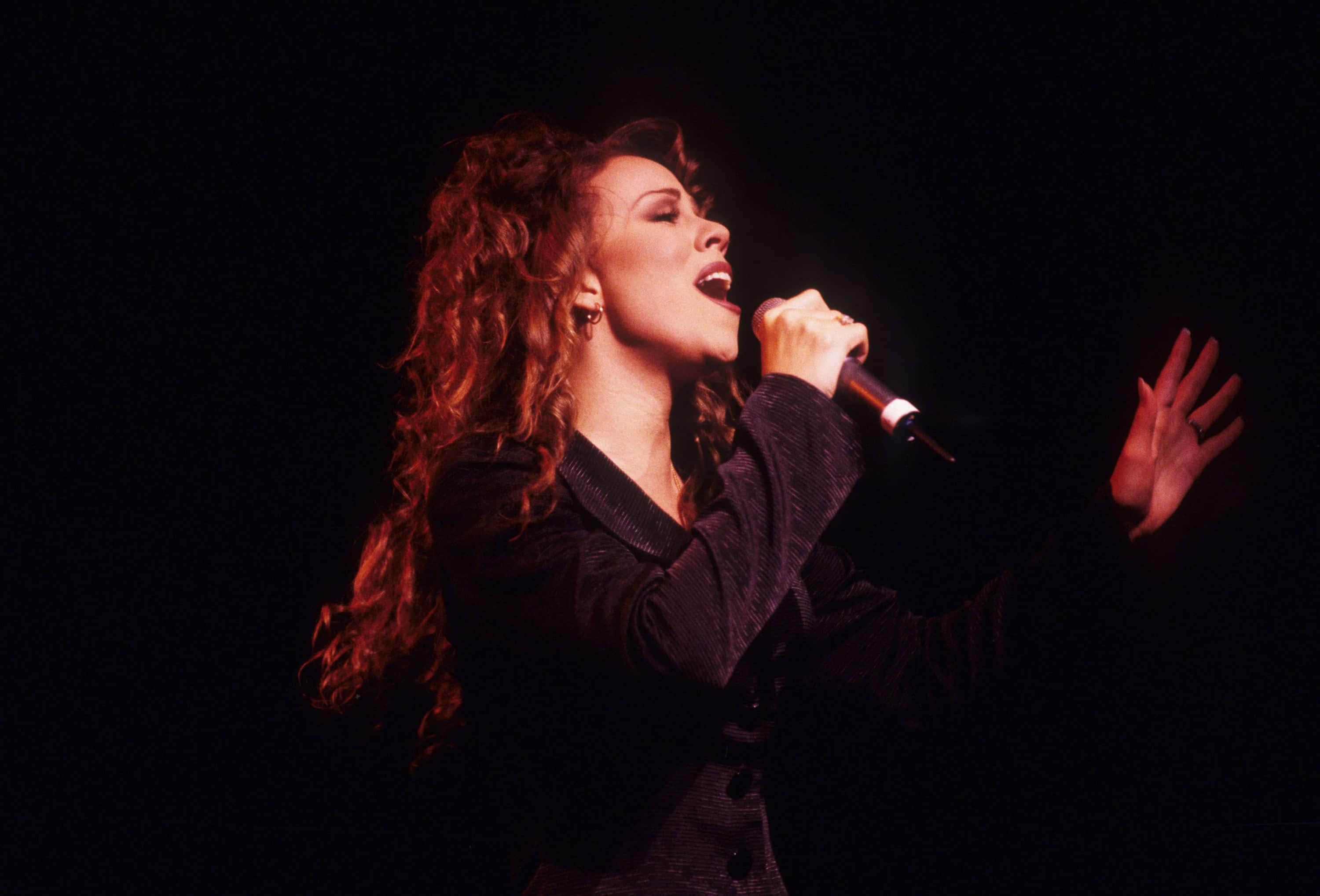 Mariah Carey wearing black jacket is performing live on stage