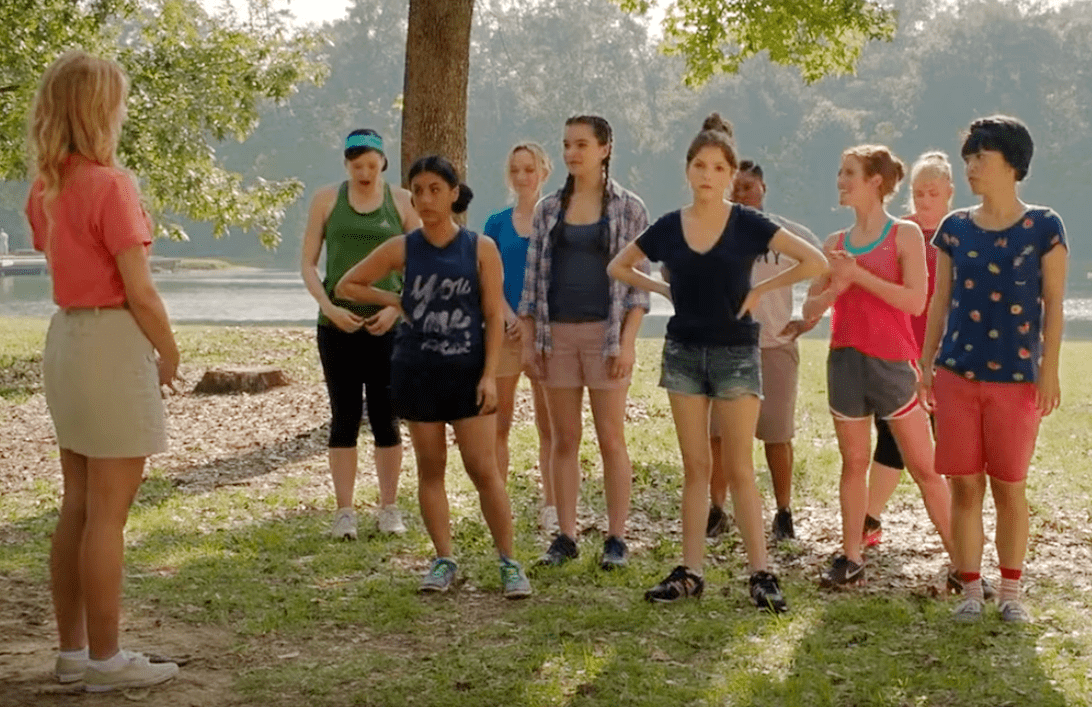Screenshot from the movie Pitch Perfect depicting teenagers standing in front of a woman ina park