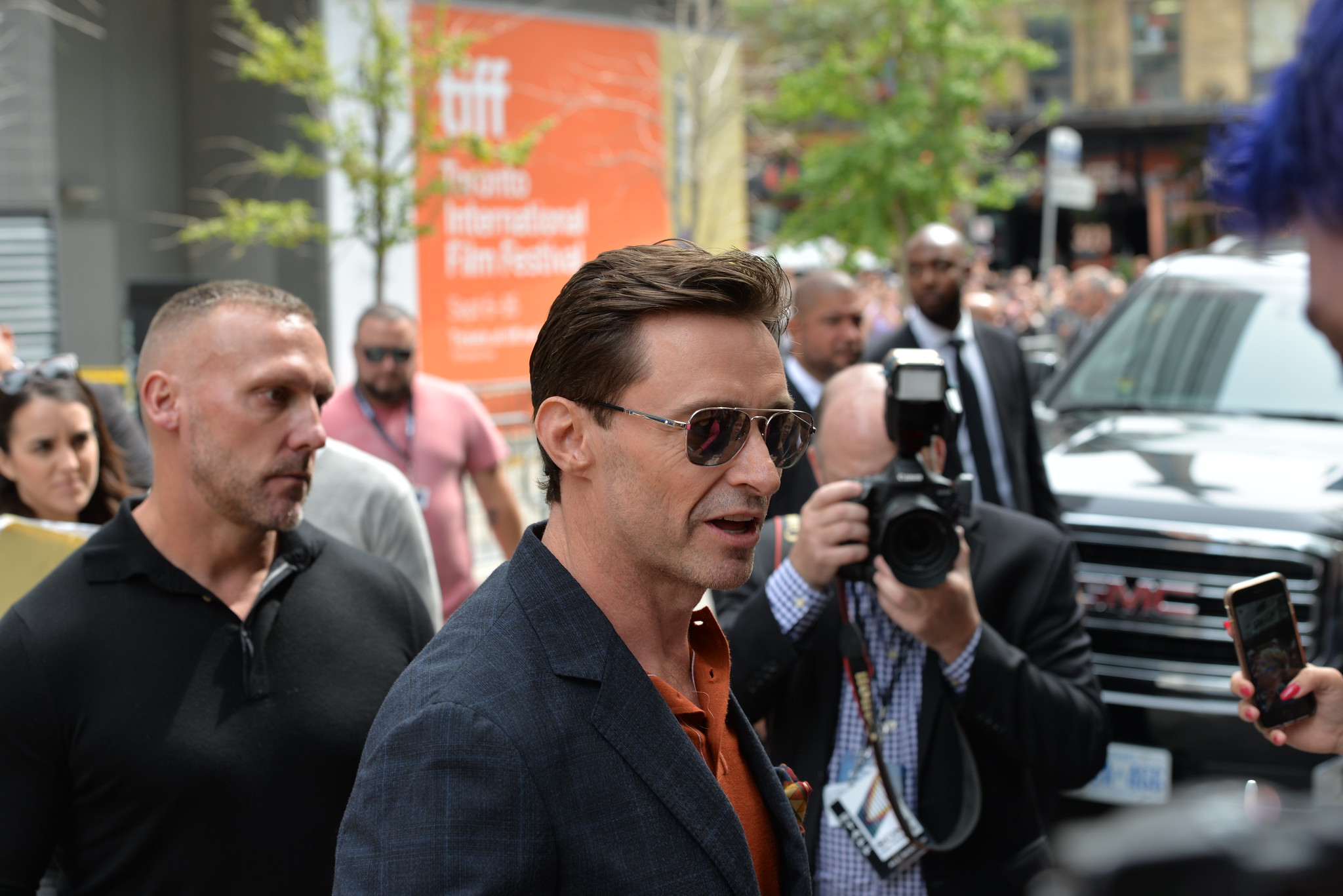 Hugh Jackman wearing an orange shirt and a pair of sunglasses