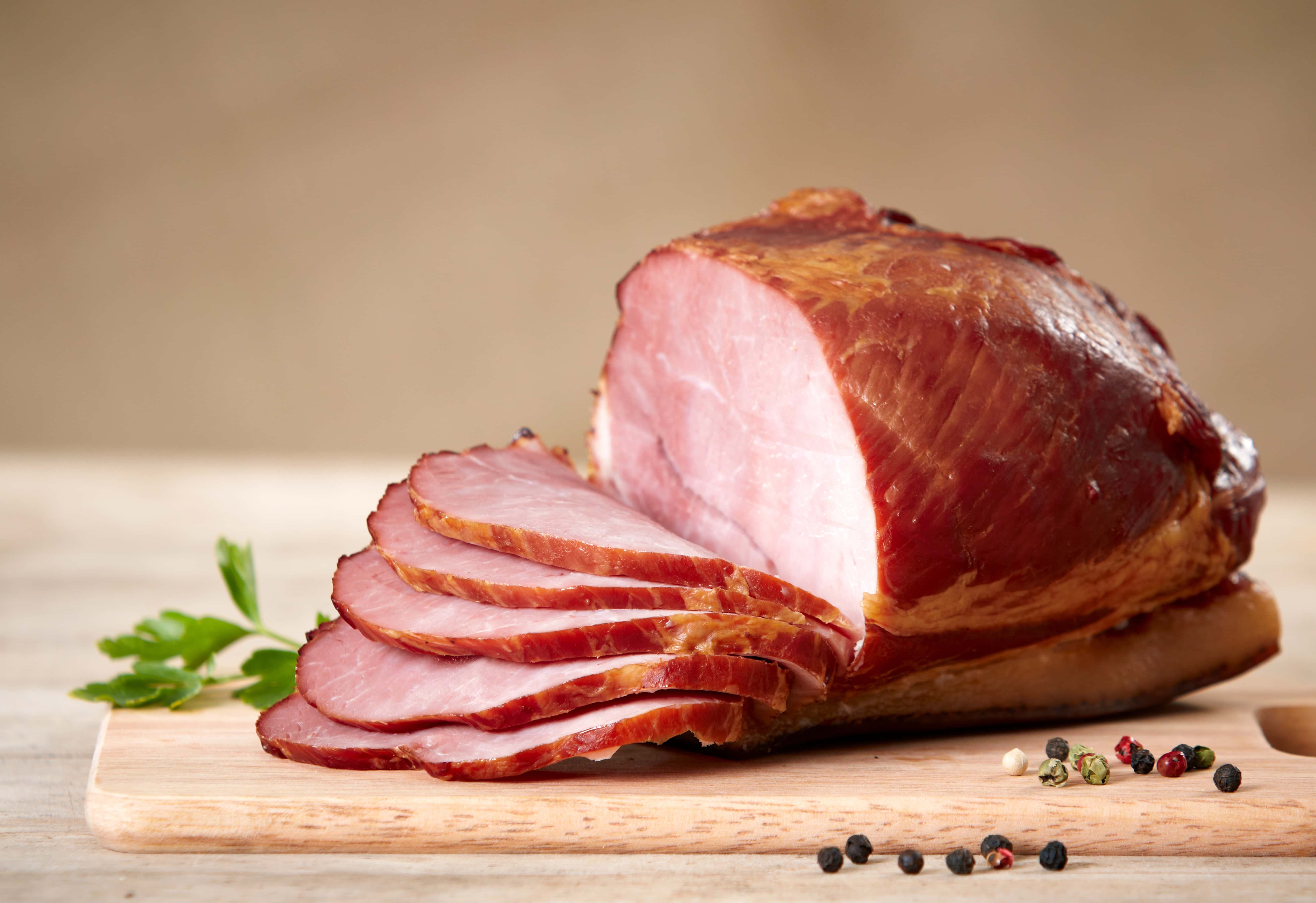 Partially sliced smoked ham on wooden cutting board