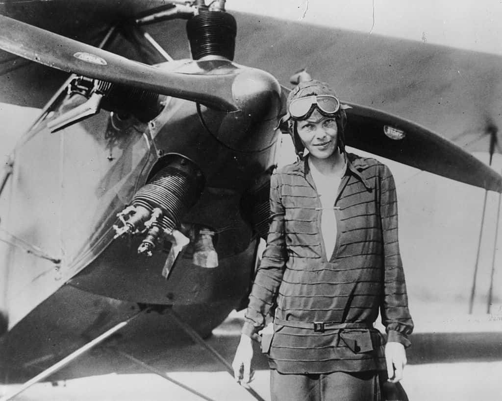 Amelia Earhart stands in front of her bi-plane called