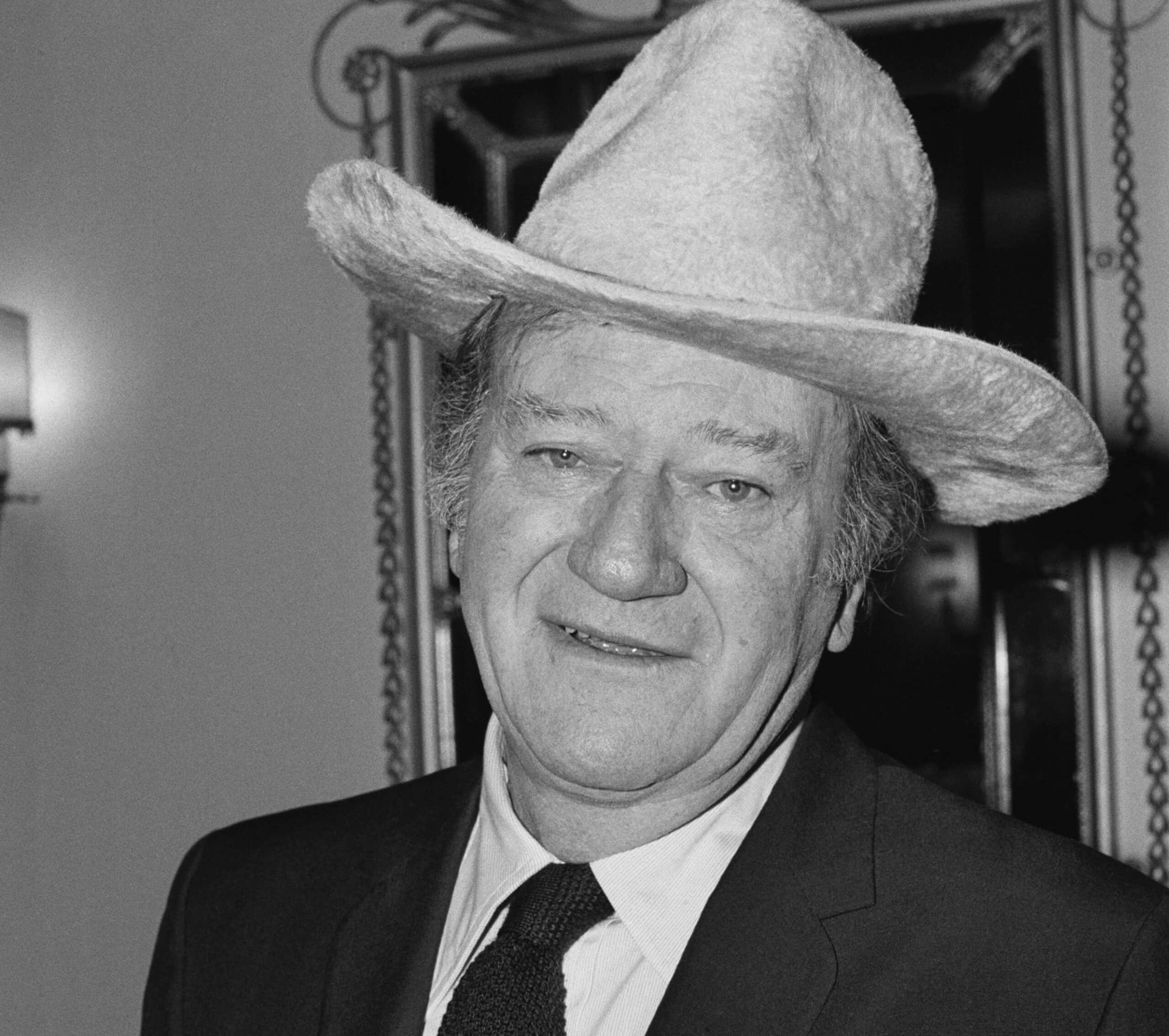 American actor and filmmaker John Wayne wearing cowboy hat and a black suit