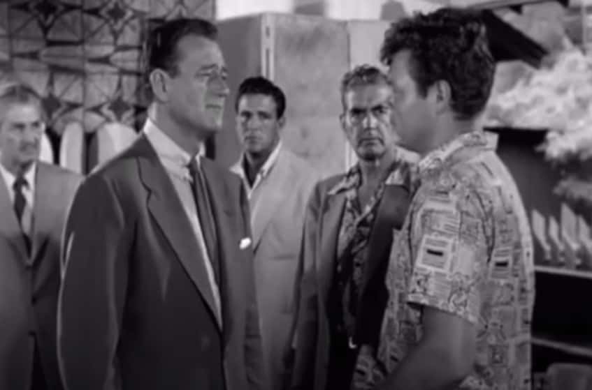 Screenshot from the movie Big Jim McLain, Actor John Wayne wearing dark suit next to the actor James Arness