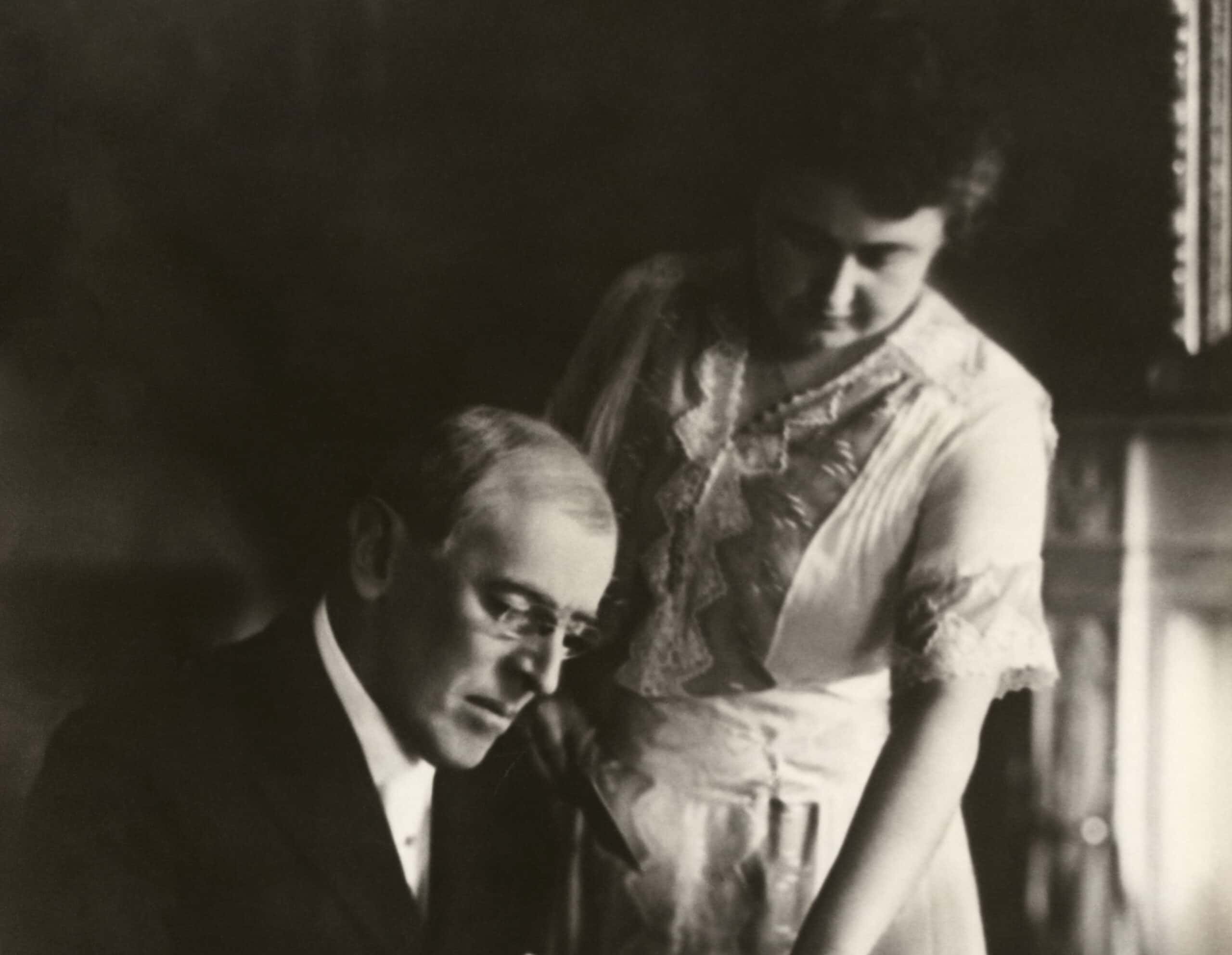 President Woodrow Wilson, seated at desk with his wife, Edith Bolling Galt, standing at his side