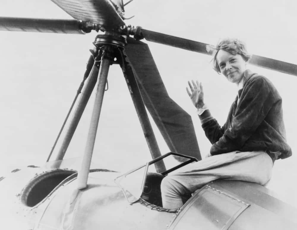 Amelia Earhart  waving, seated outside cockpit on top of an Autogiro