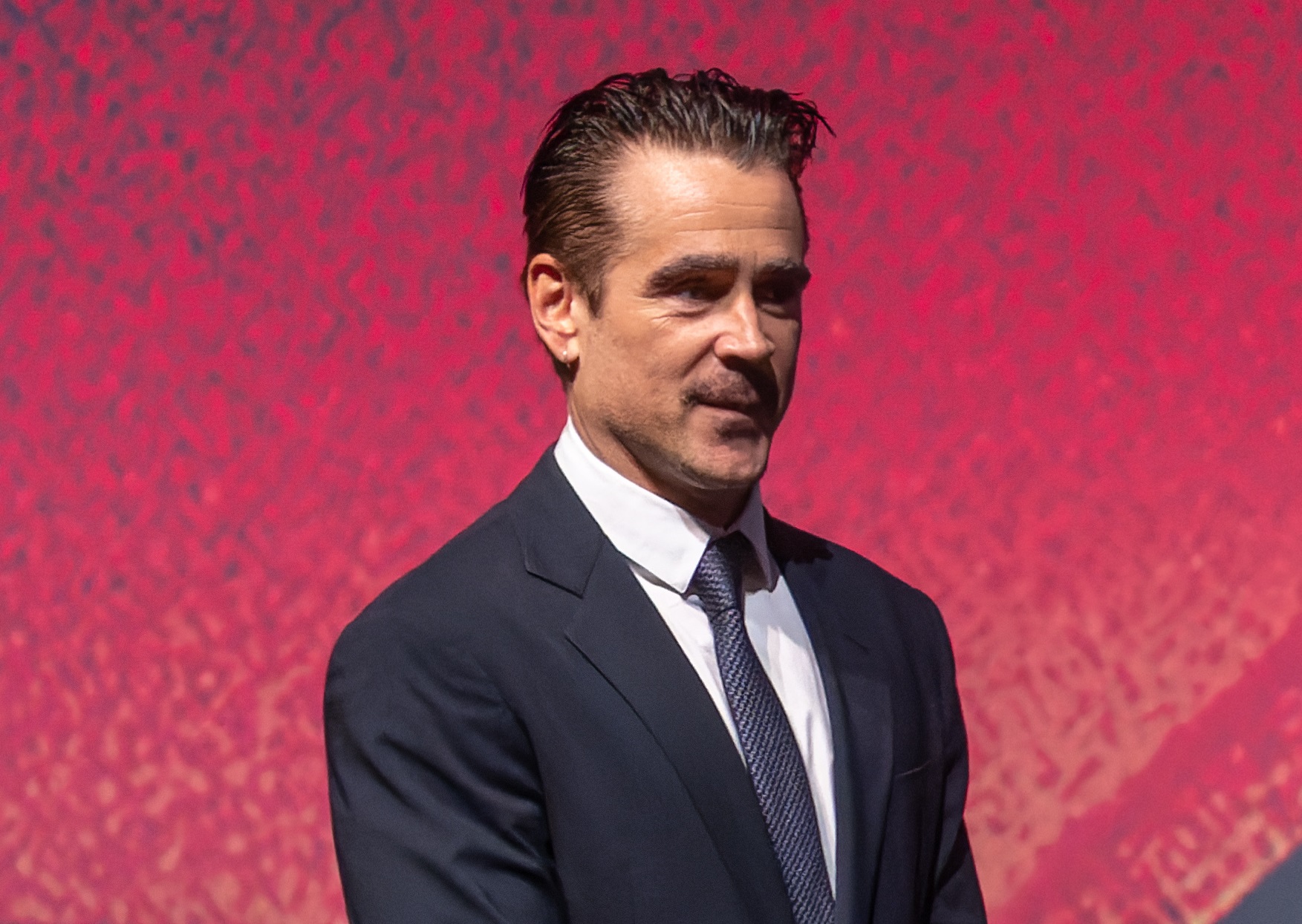 Colin Farell walking onstage and holding a microphone