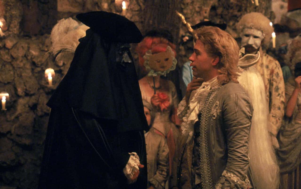 Screenshot: Wolfgang Amadeus Mozart with grey coat is talking with people - from Amadeus (1984)