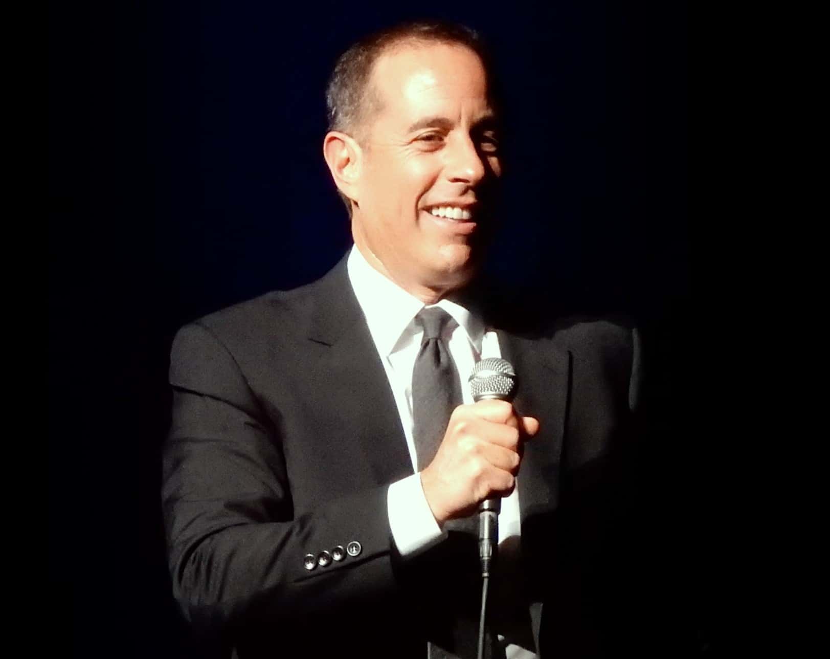 Portrait Photo of Jerry Seinfeld in dark suit performing on stage