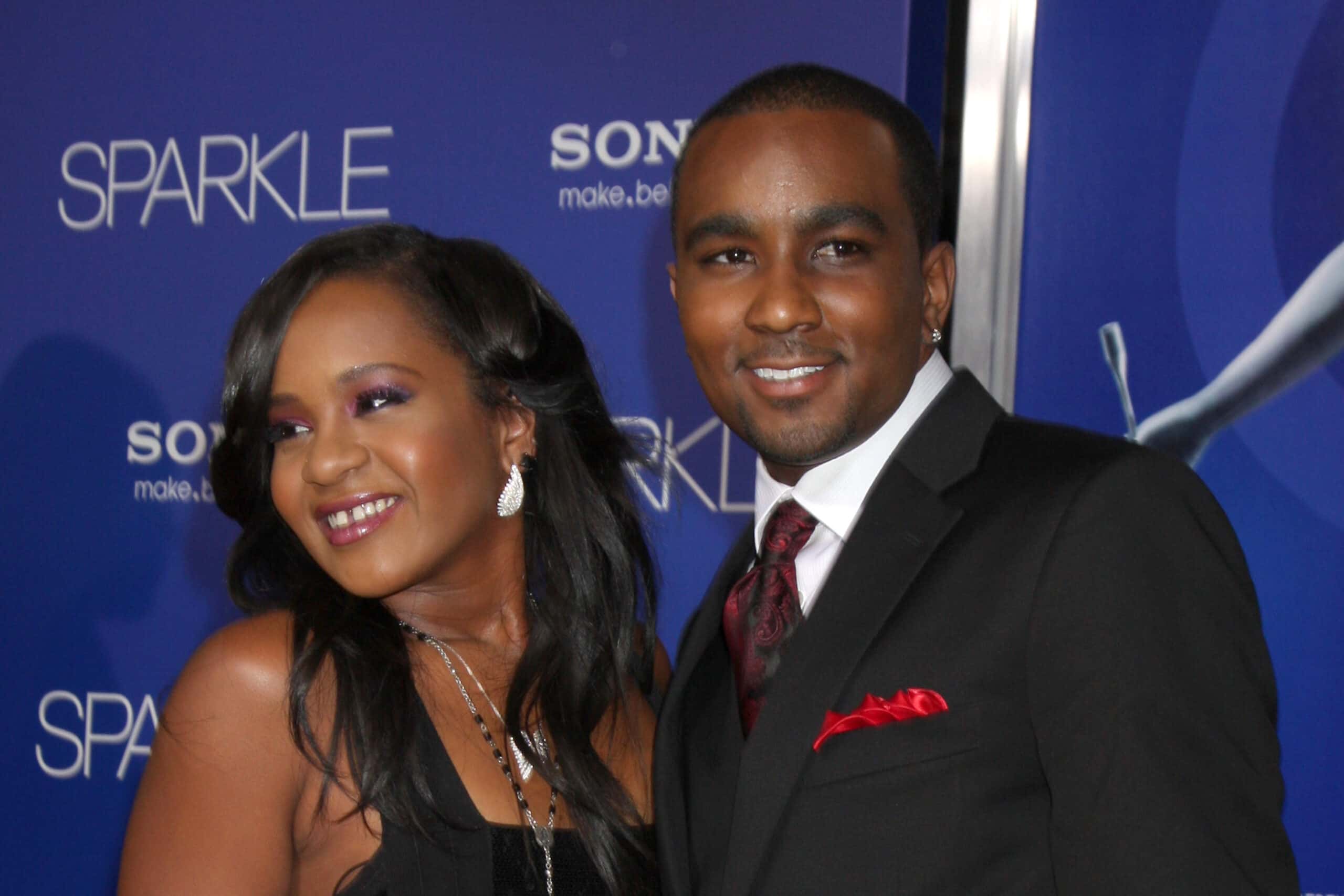 Kristina Brown in black dress and Nick Gordon in black suit are standing and smiling - 2012
