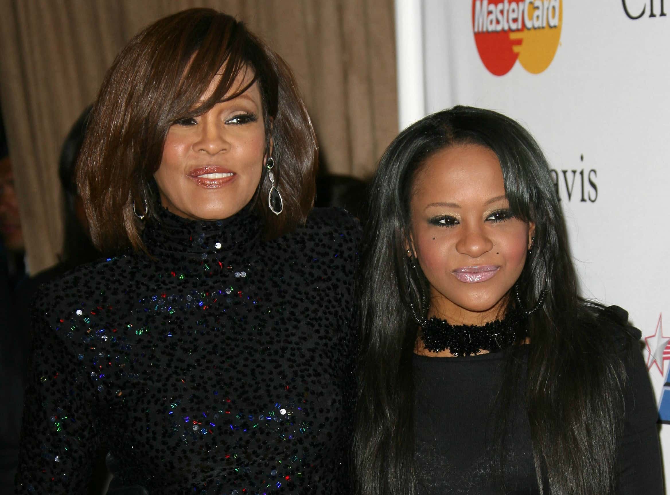 Whitney Houston and daughter Bobbi Kristina wearing black dresses are looking at side and smiling - 2011