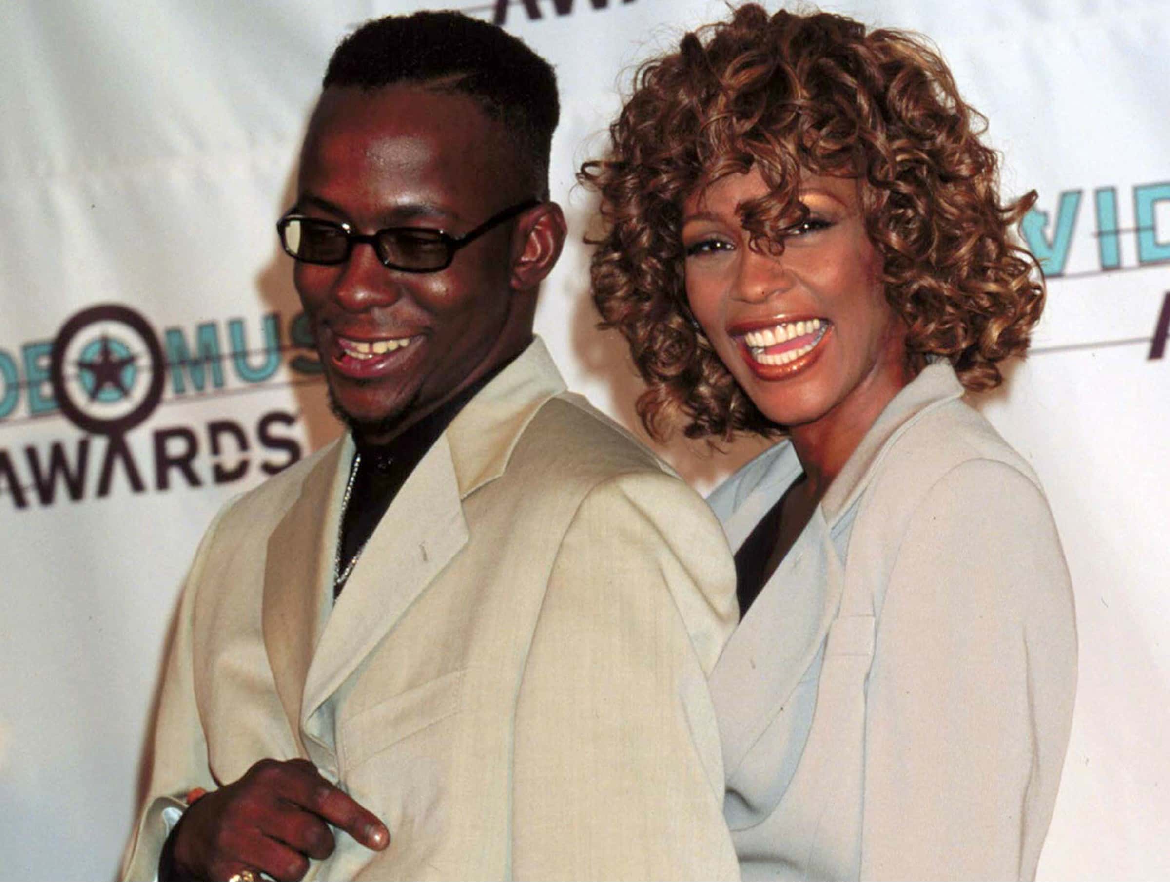 Bobby Brown and Whitney Houston wearing white suits are smiling and looking at camera - 1998
