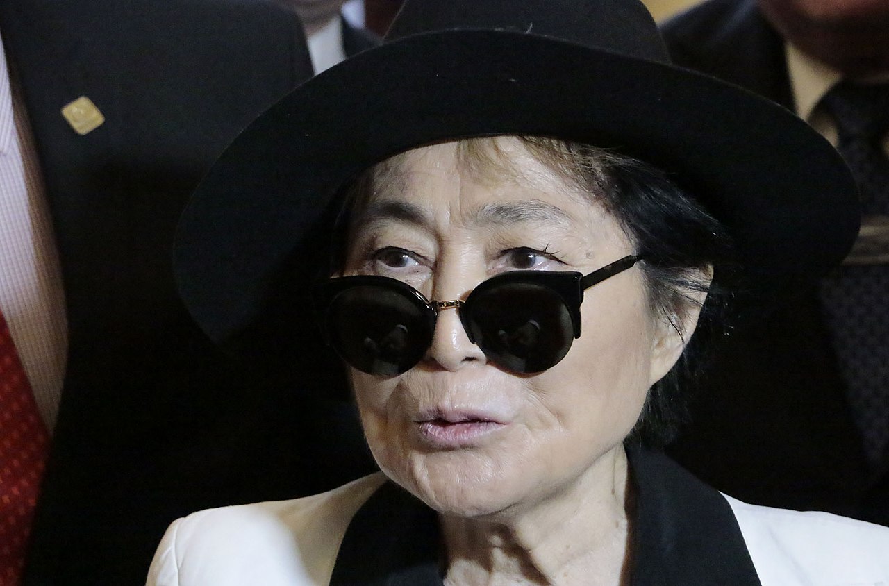 Yoko Ono in white outfit and dark sunglasses