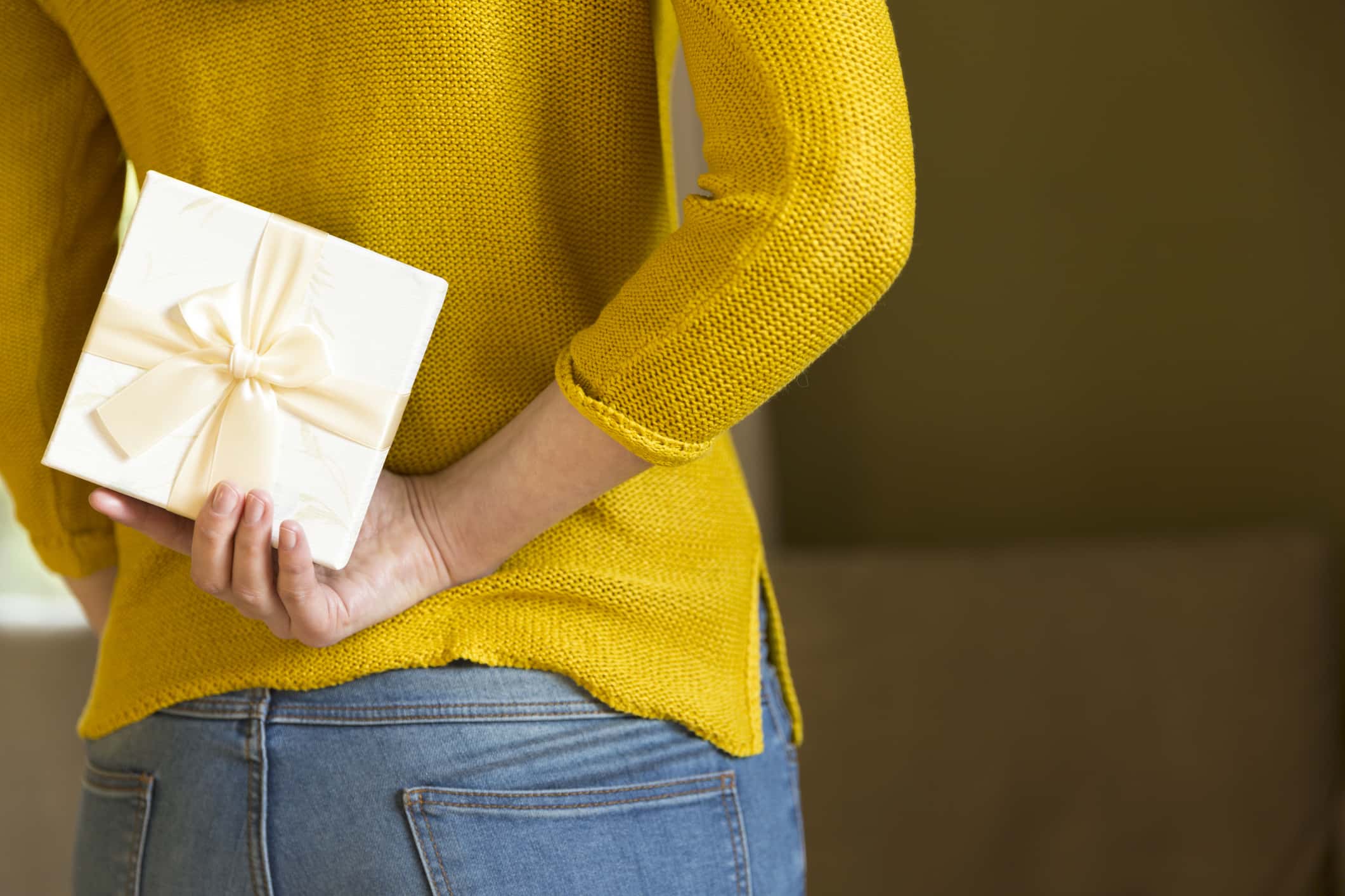 Woman hiding gift box behind her back.