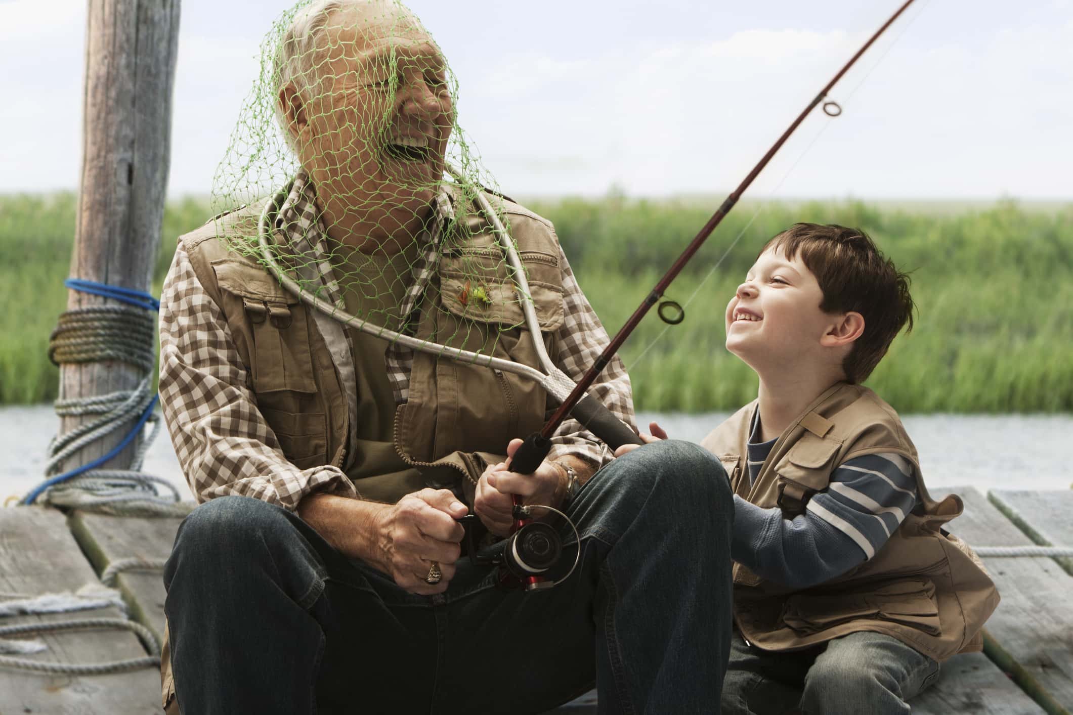 Caucasian boy putting fishing net over grandfather's head.