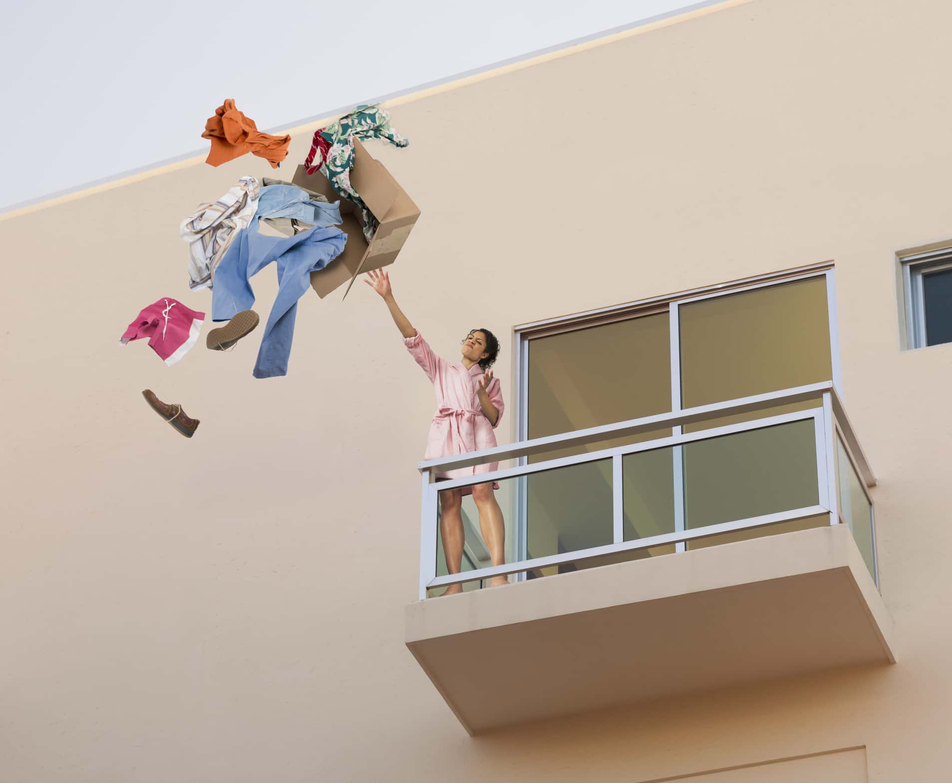 Mixed race woman throwing clothes off balcony.
