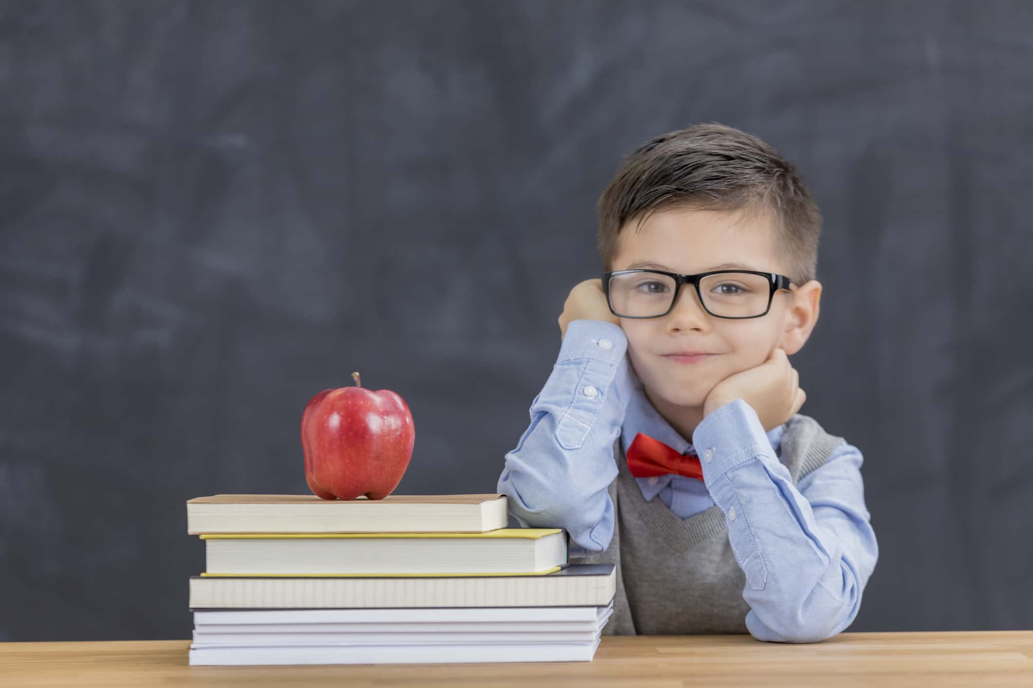 Cute boy with stack of books in the classroom.