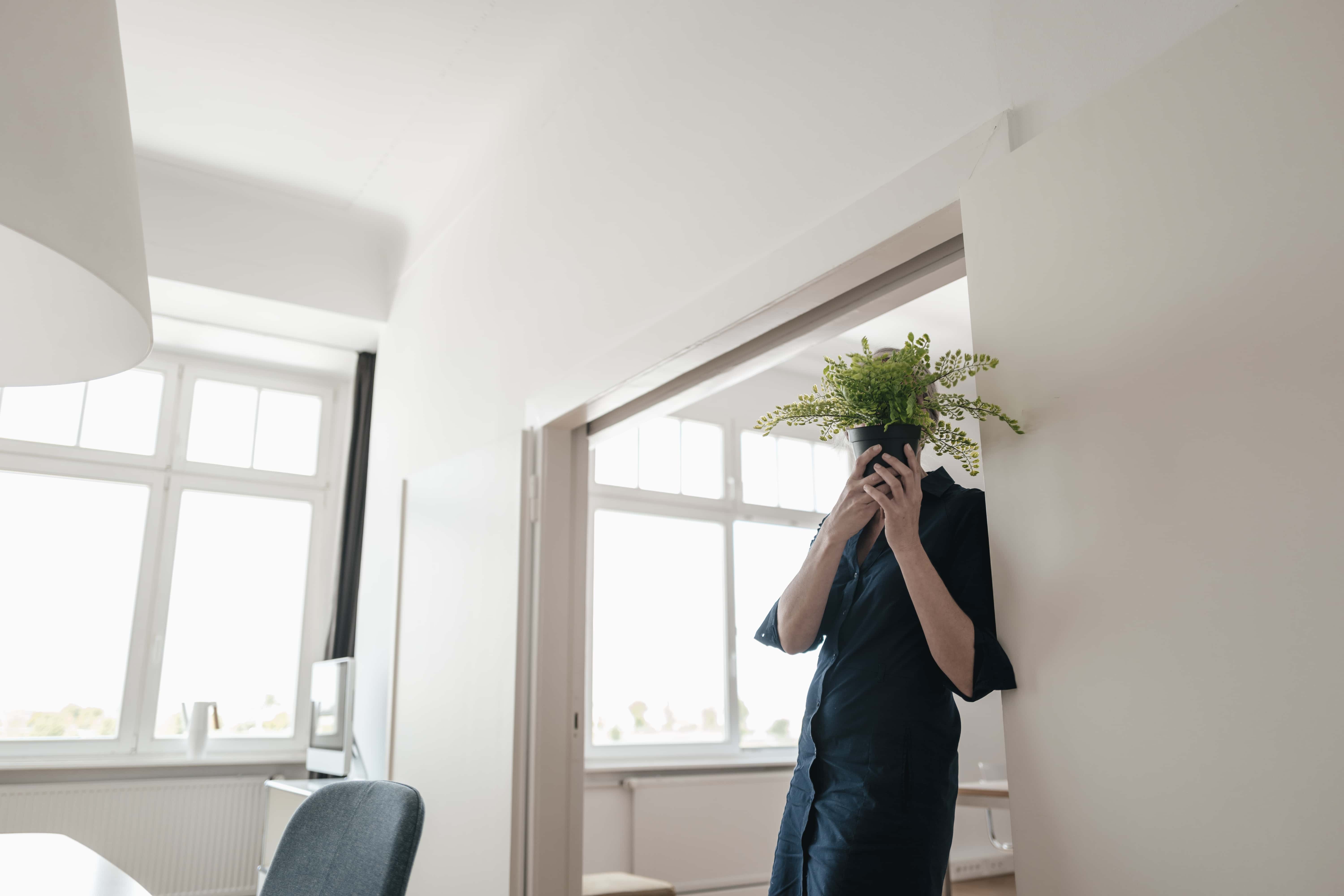 Businesswoman hiding behind plant in office