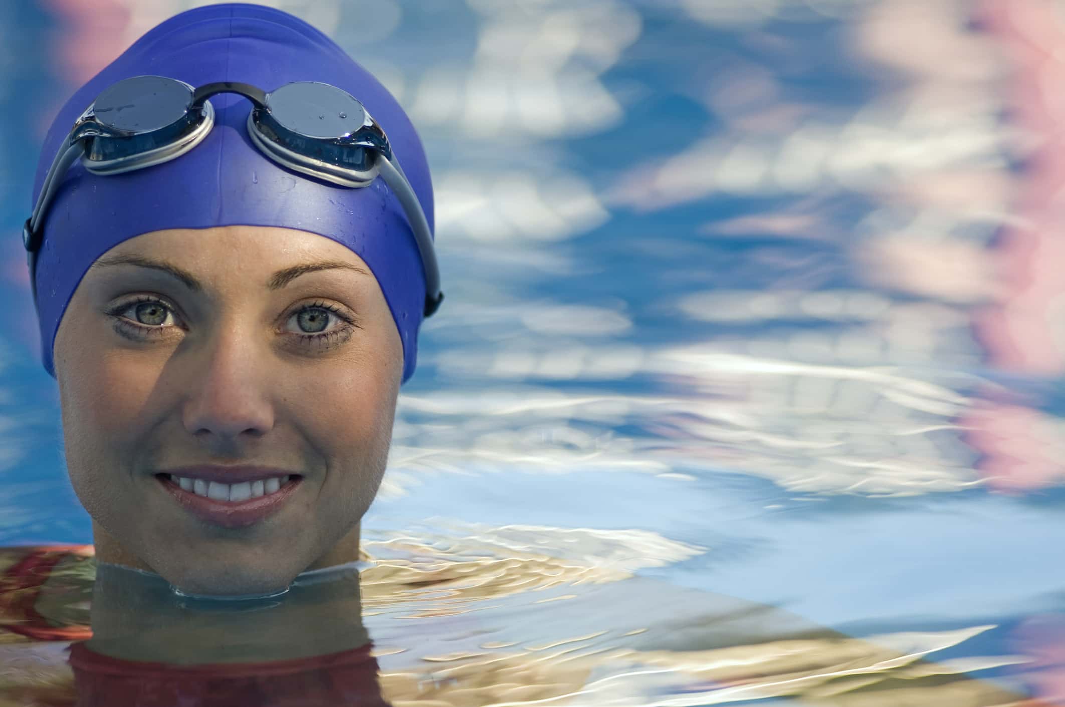 Close up of woman with swimming cap and goggles in water.