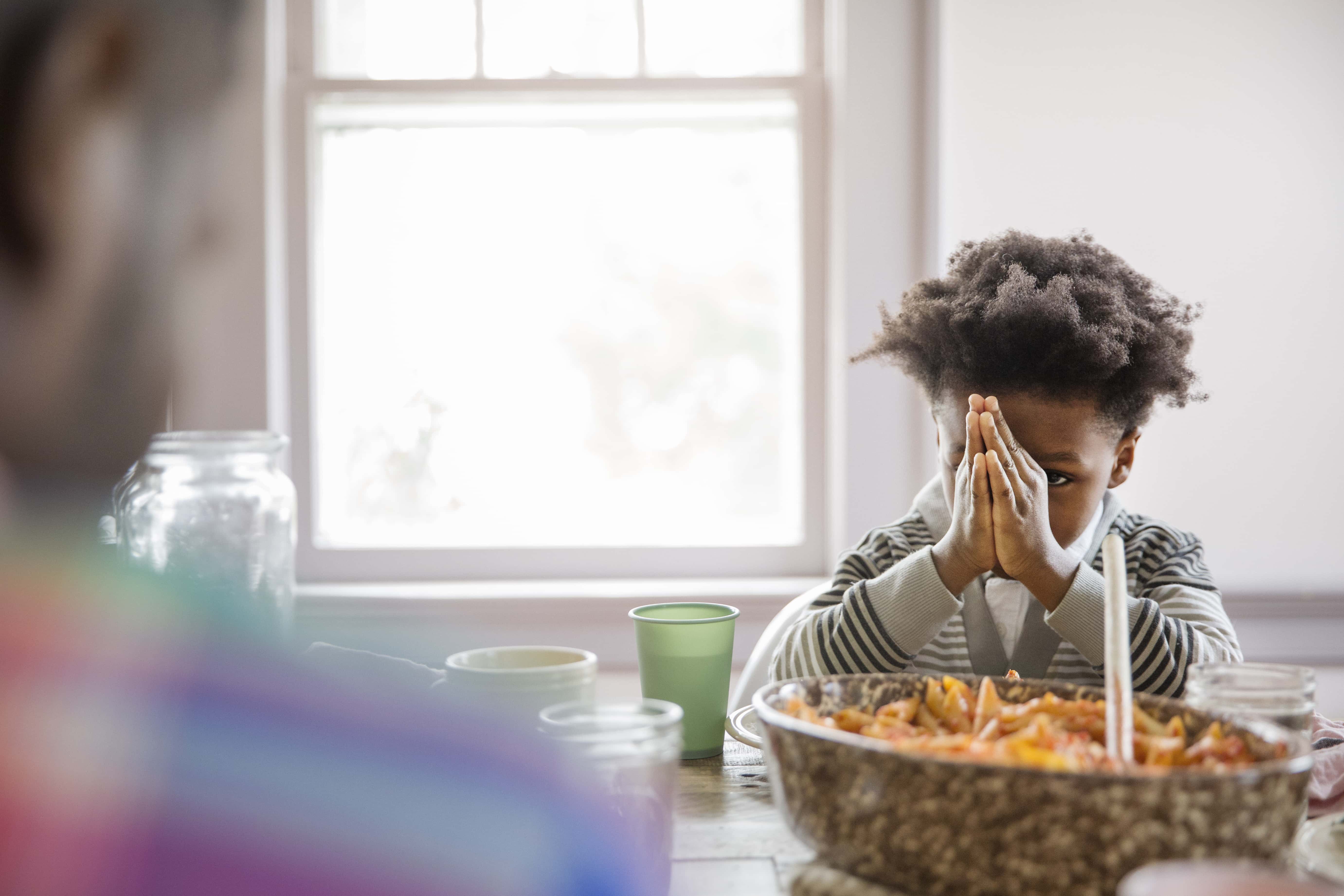 Boy looking at father while praying at dining table.