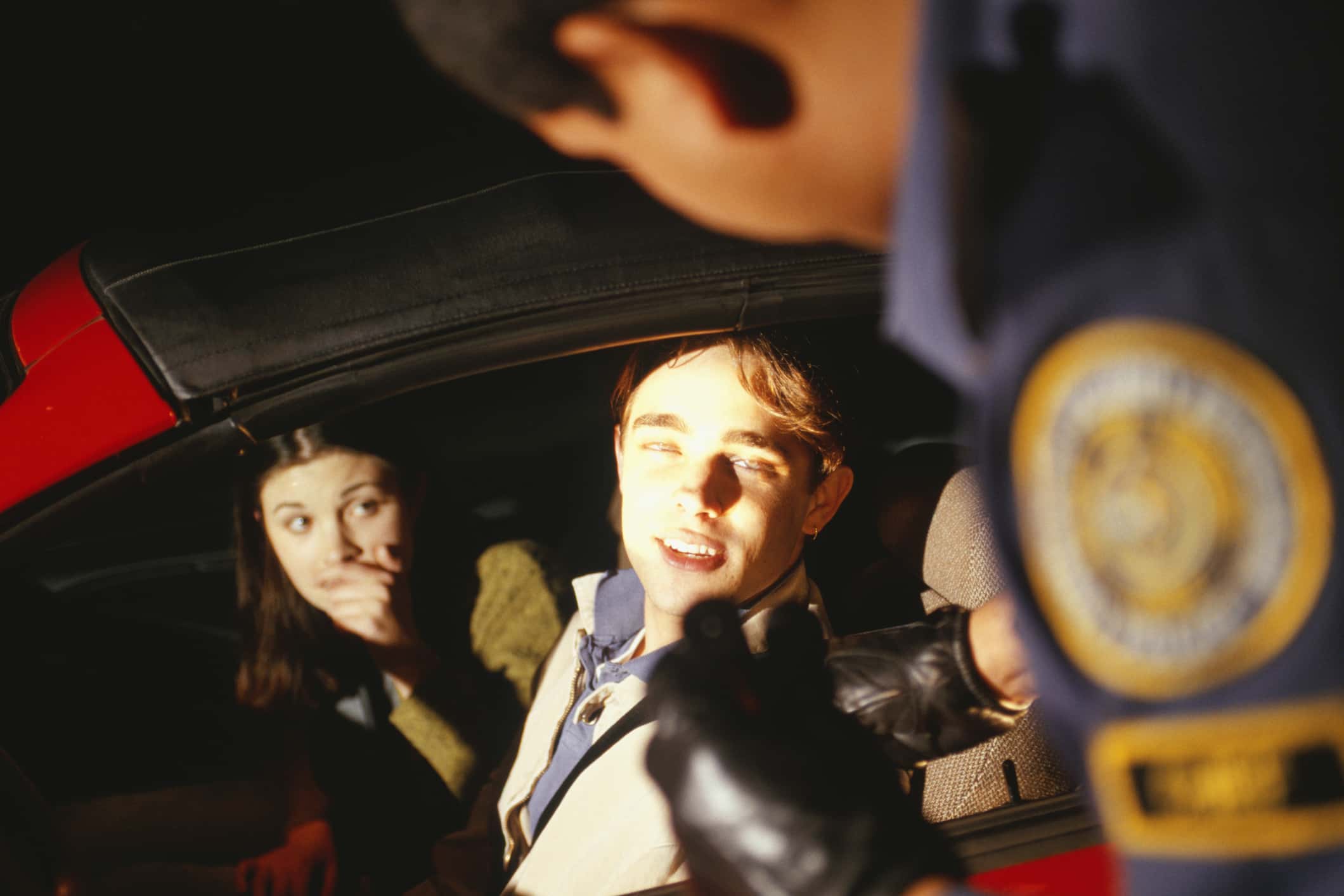 Police officer stopping couple in red car.