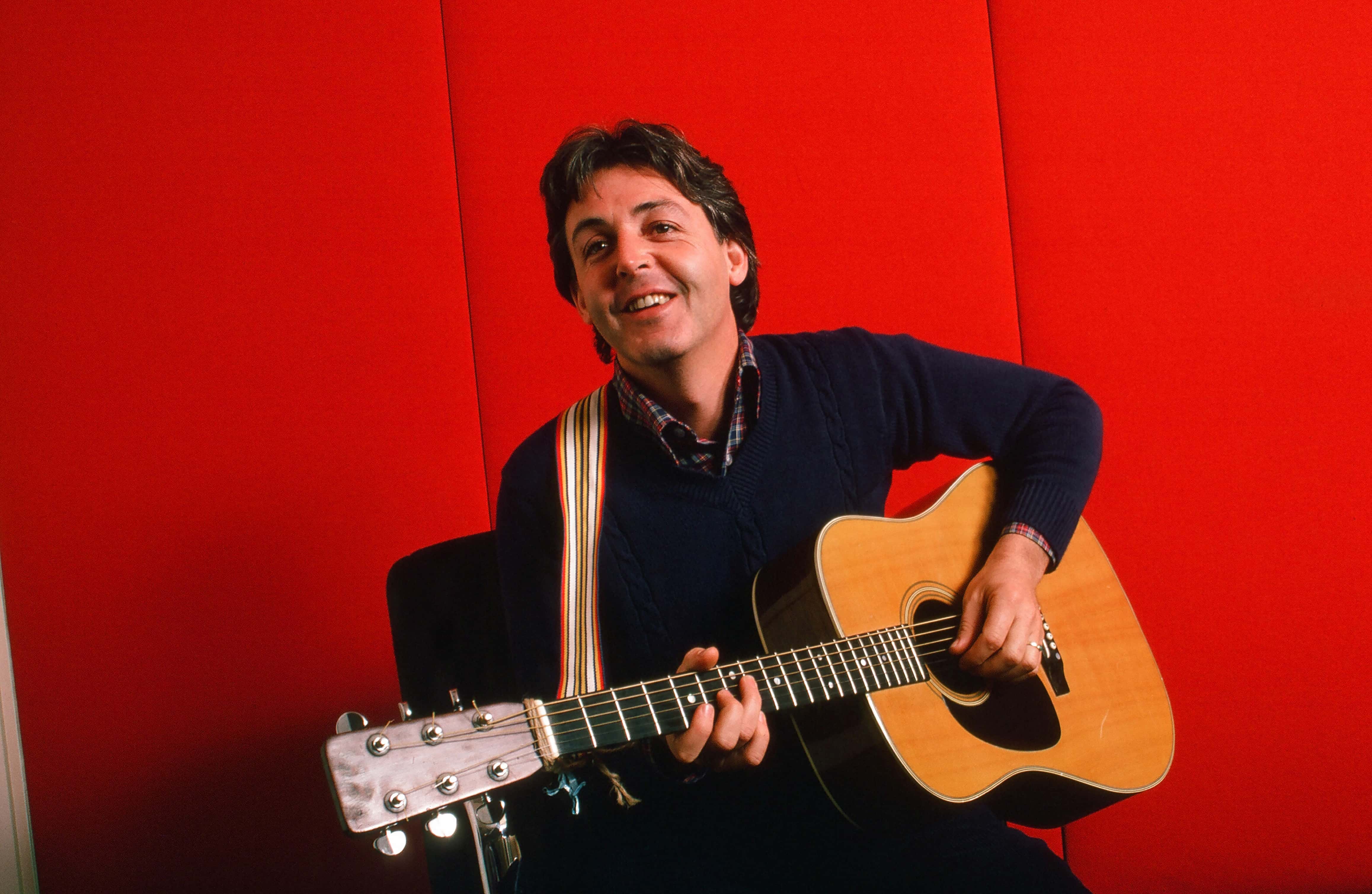 Portrait of British musician Paul McCartney as he plays acoustic guitar