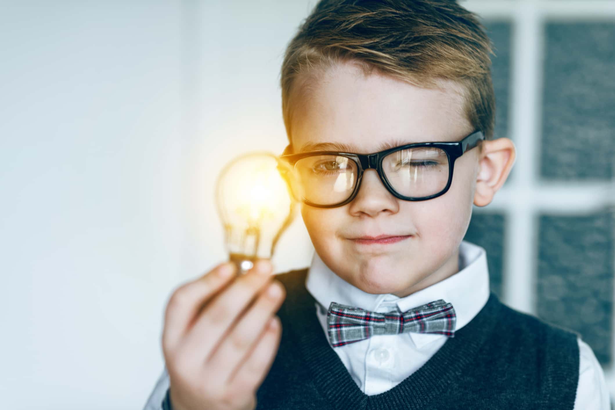 Boy with glasses and bow tie looks at glowing light bulb and gets an idea.
