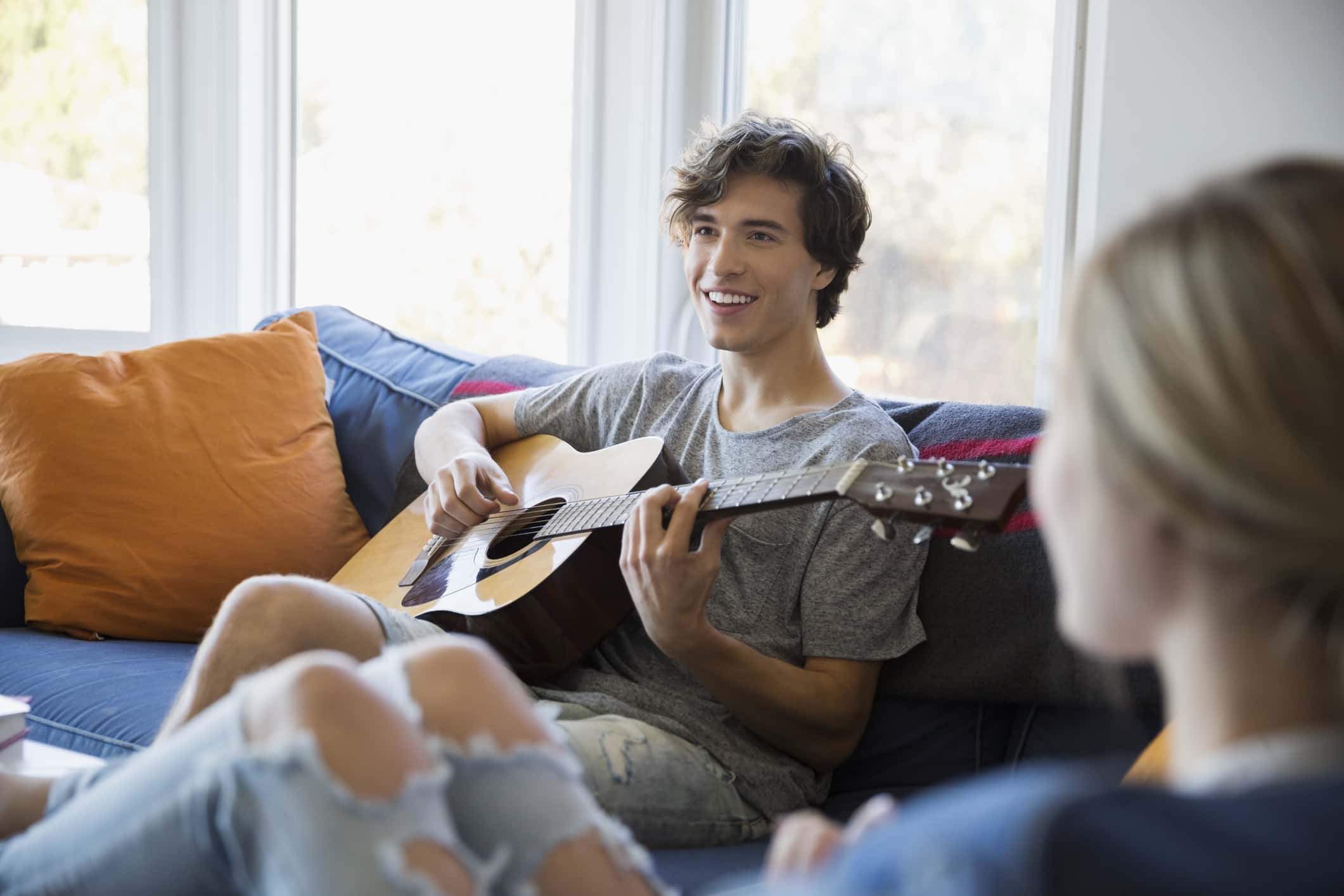 Young couple relaxing playing guitar on living room sofa.
