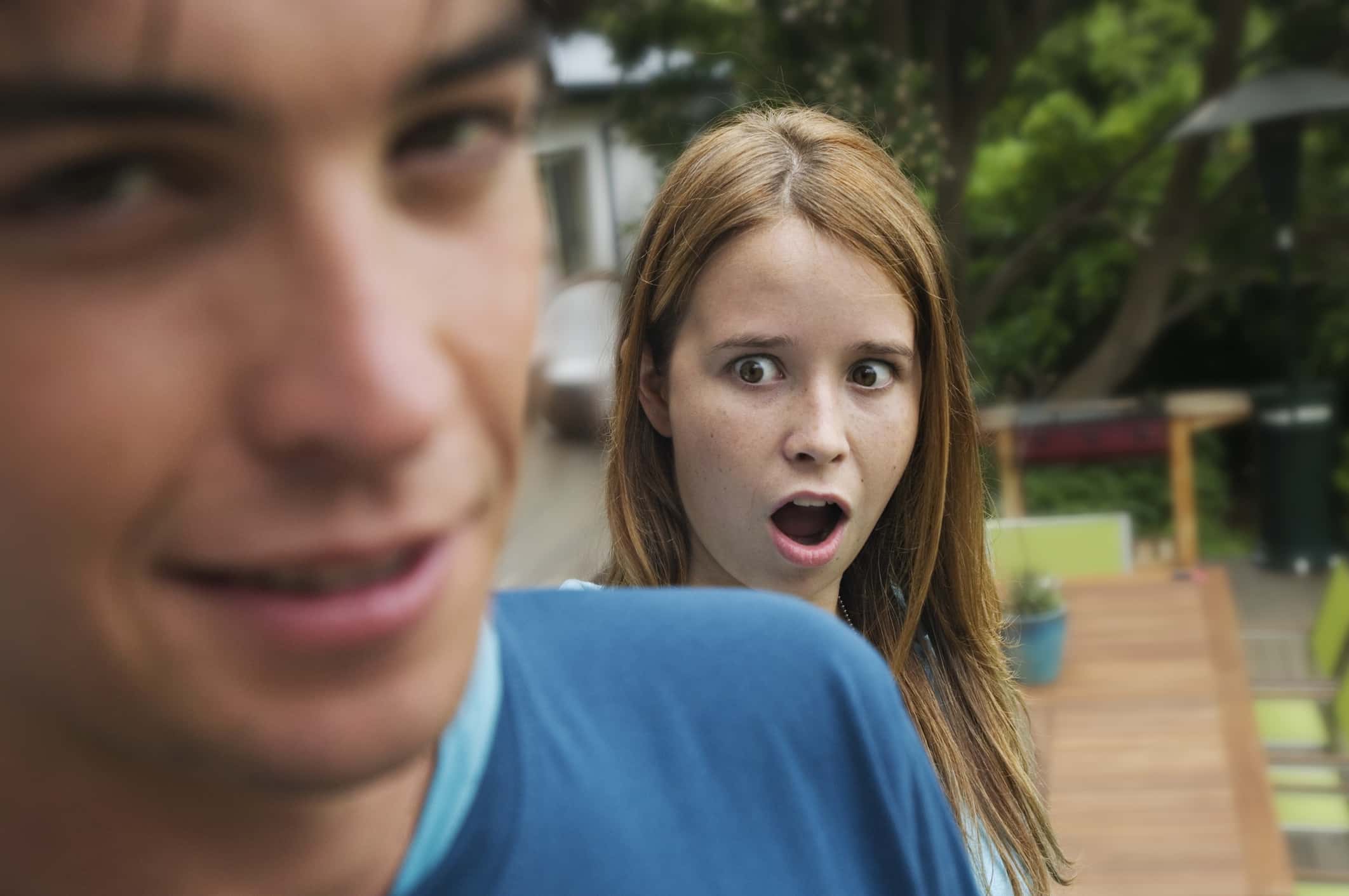 Surprised teenage girl with open mouth standing behind teenage boy.