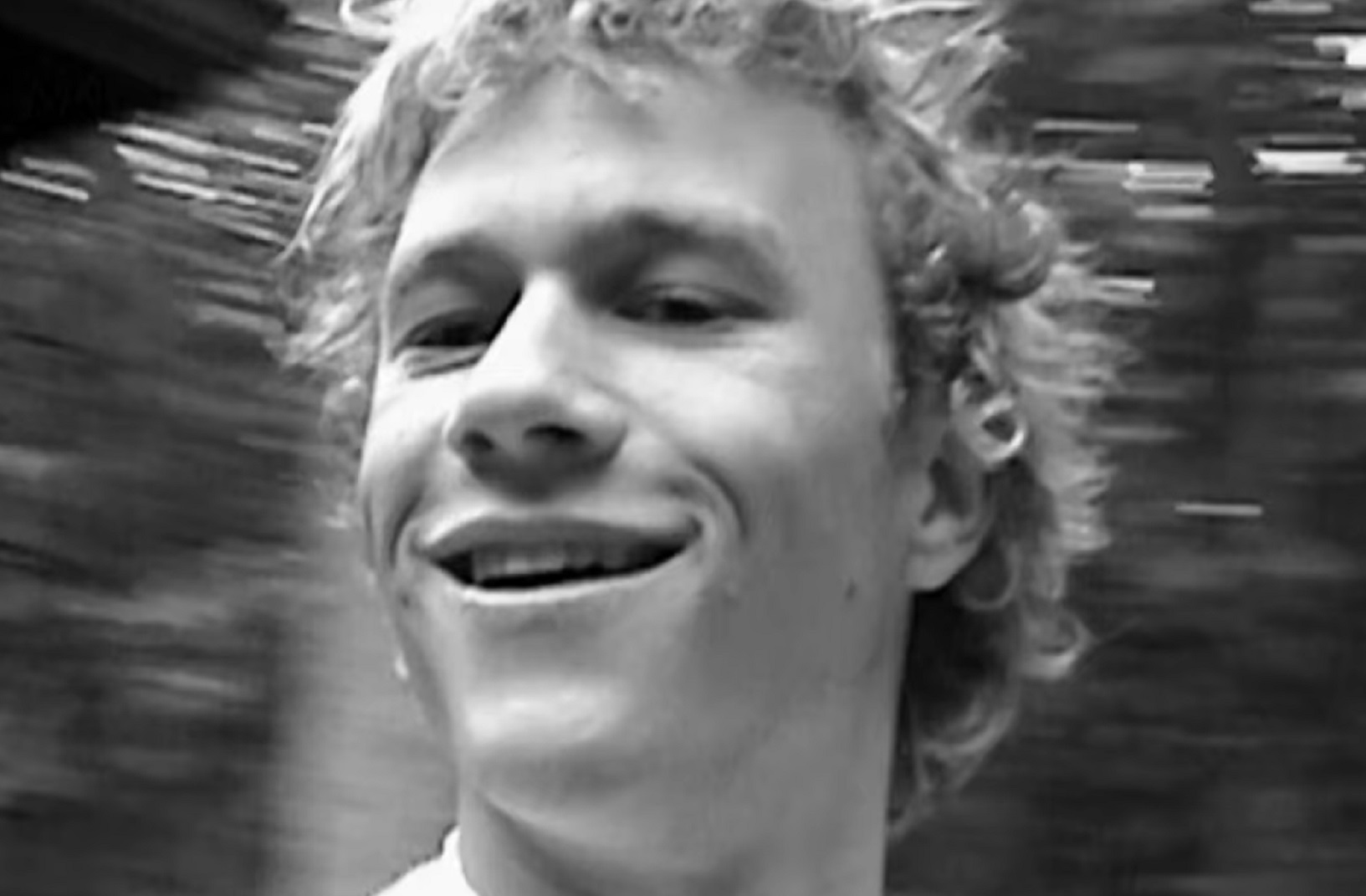 Screenshot: B&W close up photo of Heath Ledger smiling and looking aside.