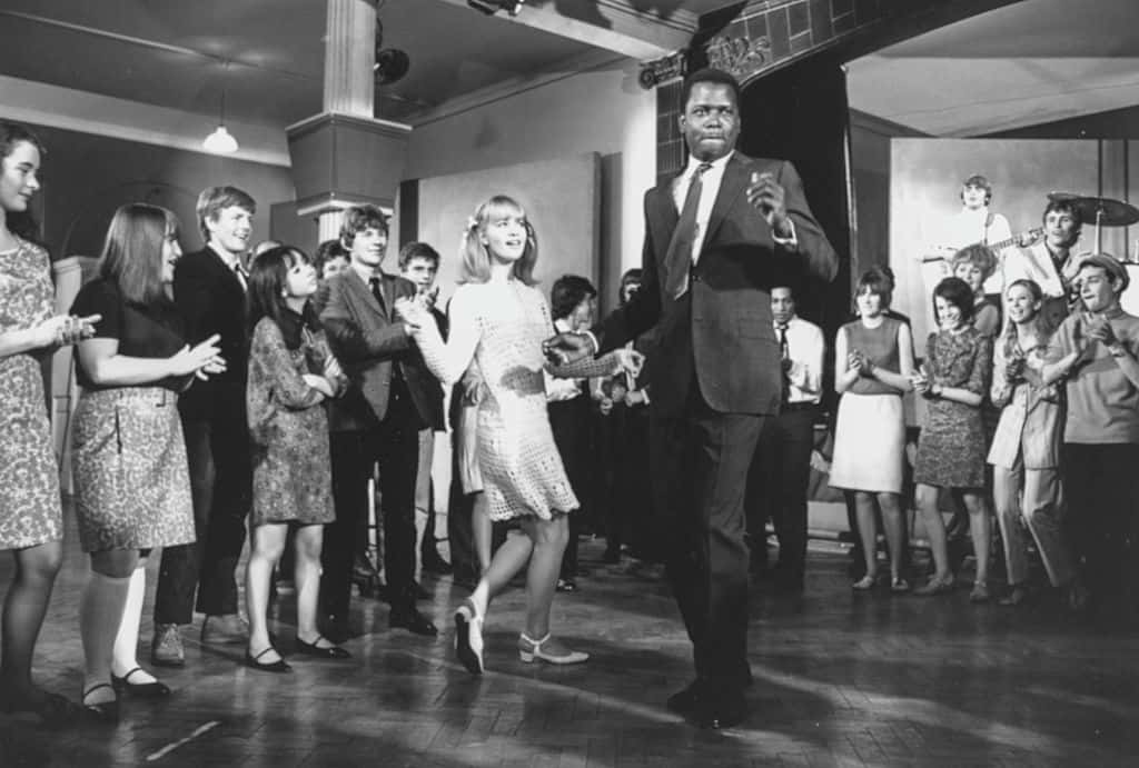 Sidney Poitier and Judy Geeson dancing in front of a crowd in a scene from the film 'To Sir, With Love'