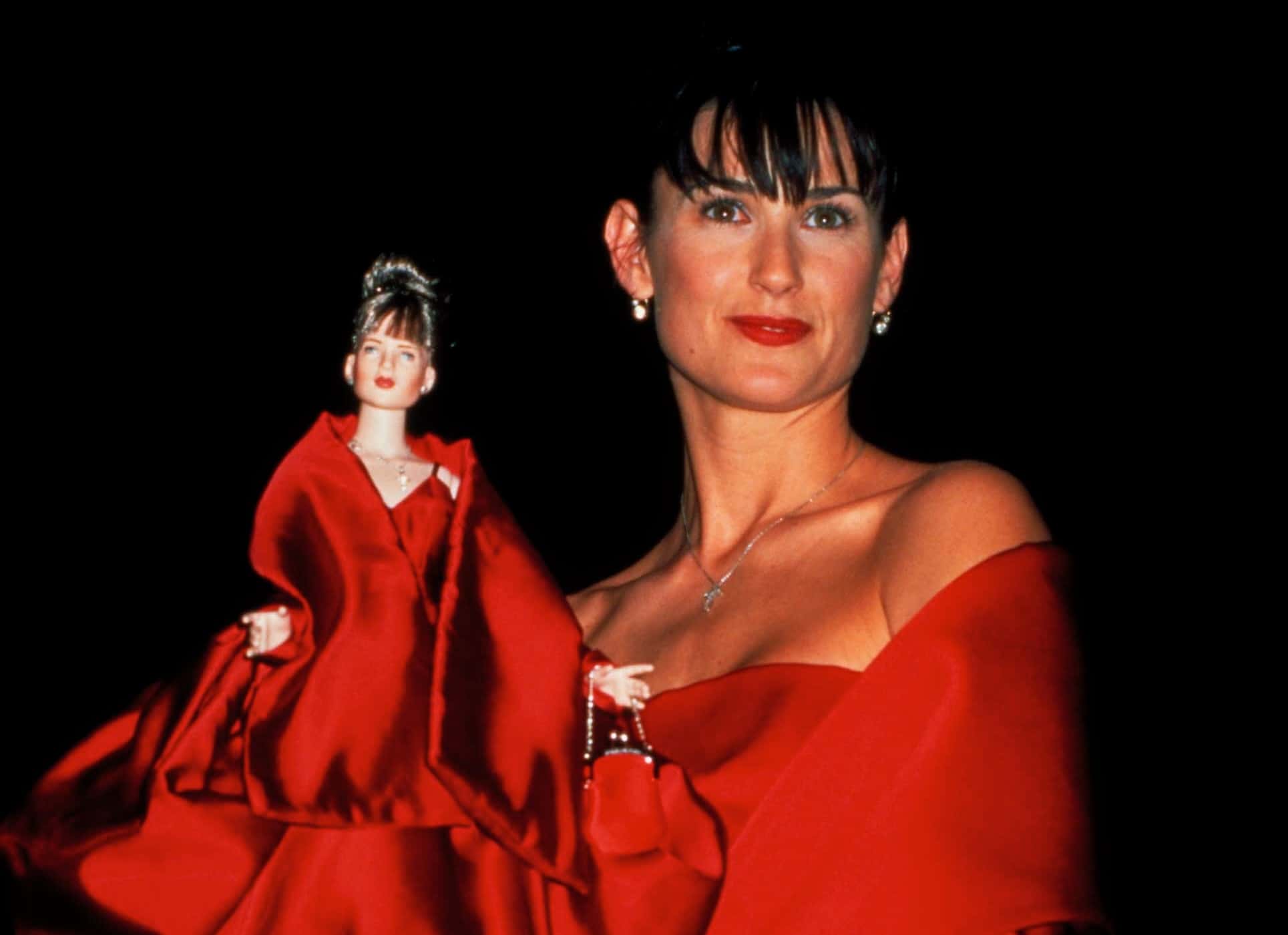 Demi Moore wearing red silk gown by Dolce & Gabbana while holding doll