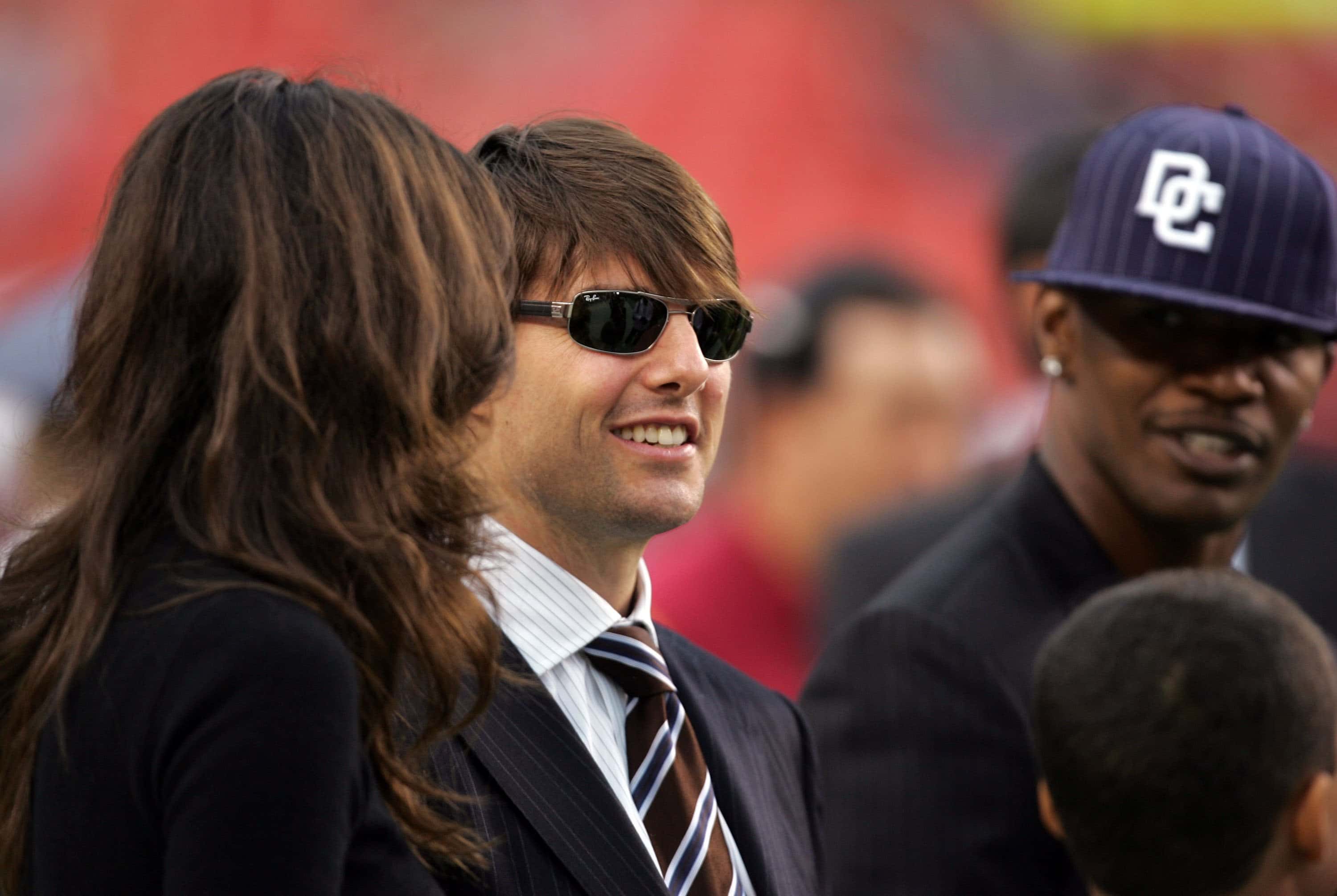 Tom Cruise, Katie Holmes and Jamie Foxx stand on the field before a game between the Minnesota Vikings and the Washington Redskins