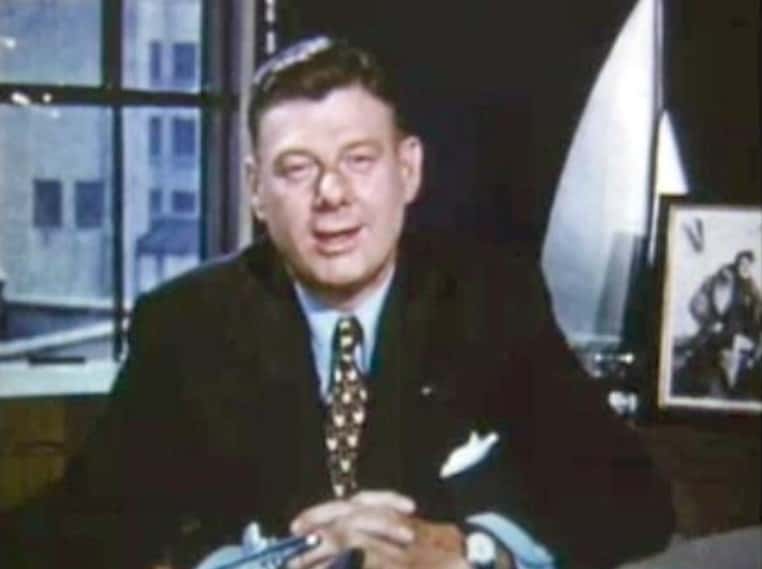 Portrait of Arthur Godfrey sitting on a desk wearing a black suit