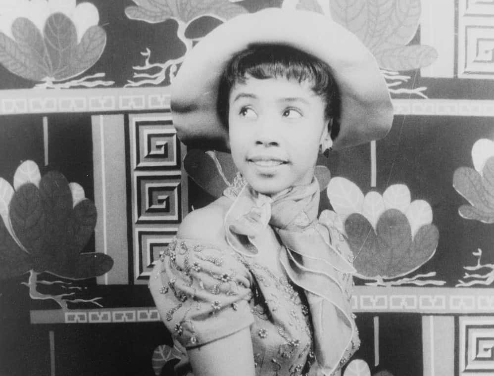 Portrait of the young actress Diahann Carroll wearing a hat on a gray gray background