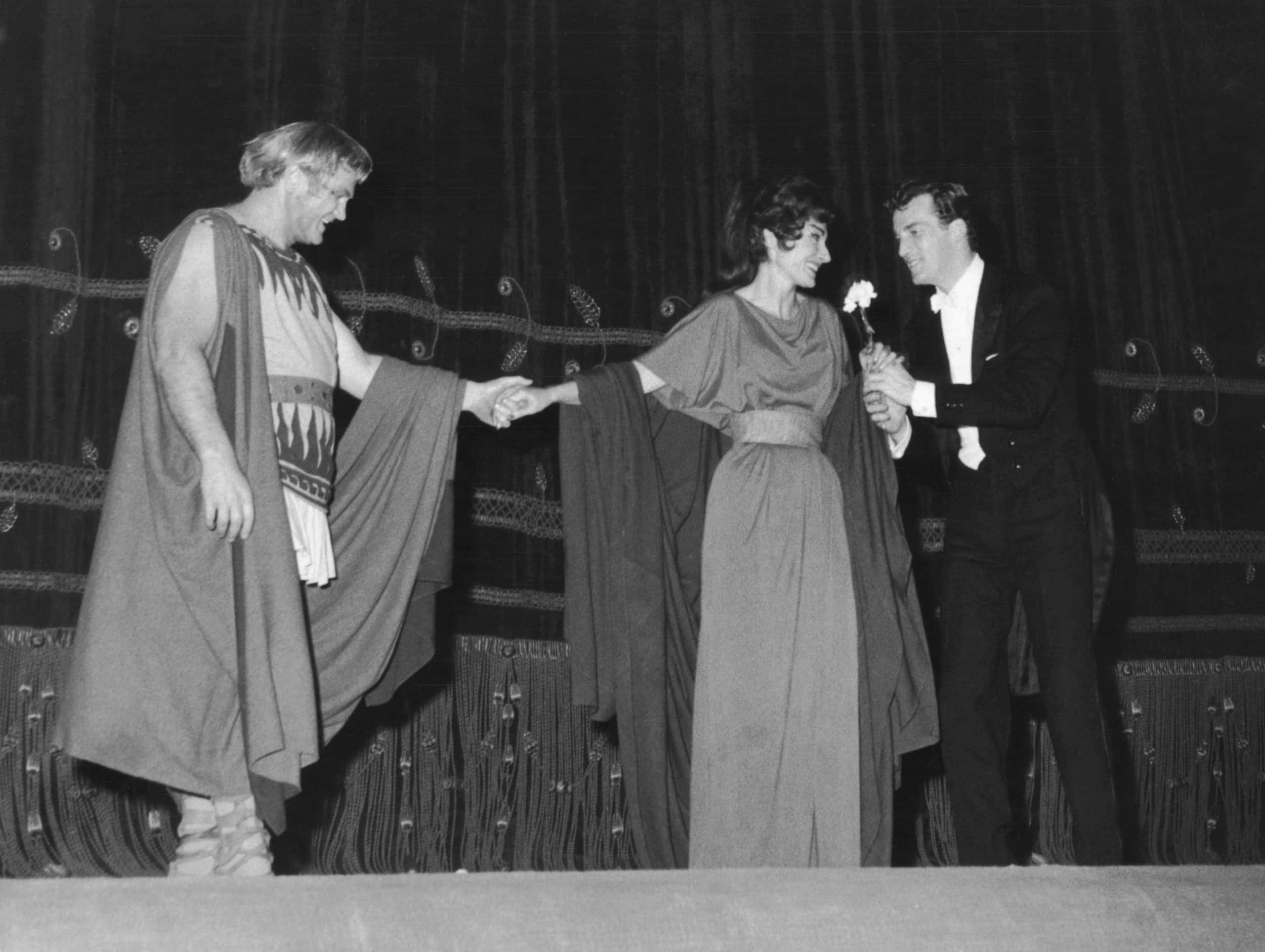 American opera singer Maria Callas (1923 - 1977) recieves a floral tribute from American conductor Thomas Schippers (1930 - 1977) as she and Canadian tenor Jon Vickers take their curtain call after a performance of Cherubini's 'Medea' at la Scala