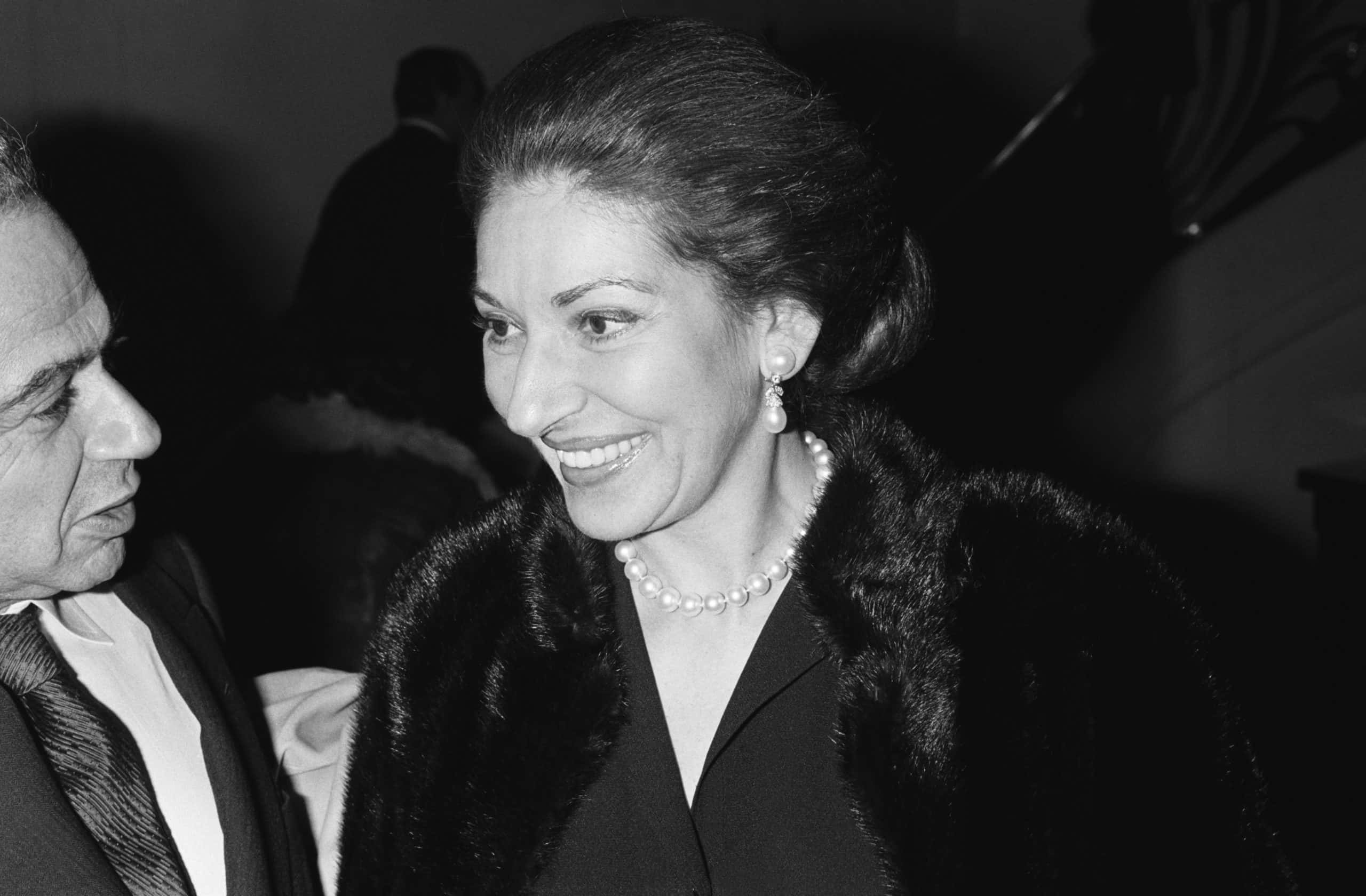 Maria Callas, American-born Greek soprano wearing a black outfit, speaking with another person