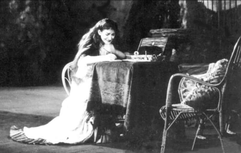 Photo of Maria Callas, performing on a stage, sitting on a chair, writhing something, crying