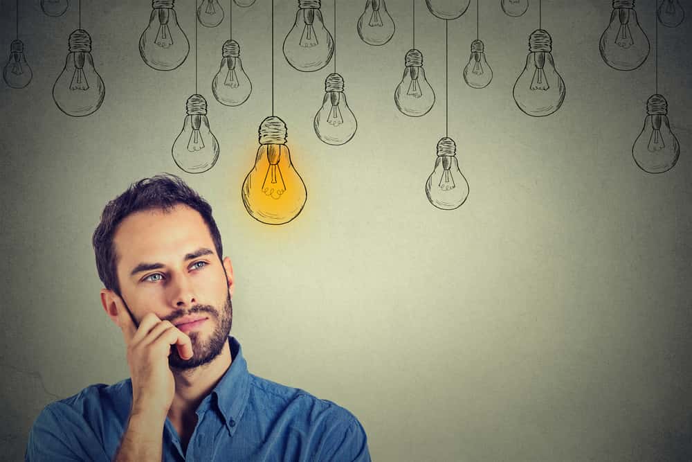 Portrait thinking handsome man looking up with idea light bulb above head isolated on gray wall background