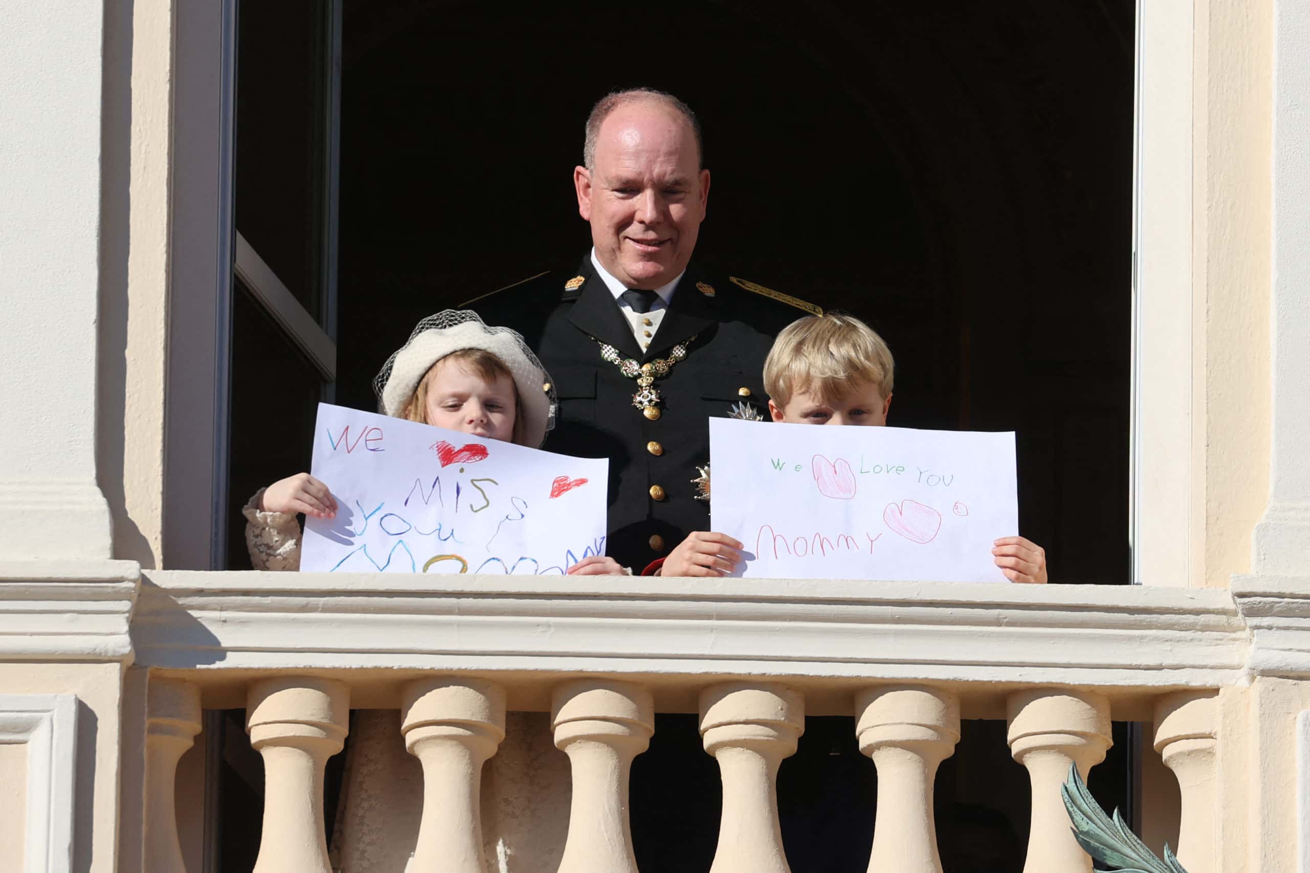Prince Albert II of Monaco, Princess Gabriella and Prince Jacques stand with a message for Princess Charlene at the balcony of Monaco